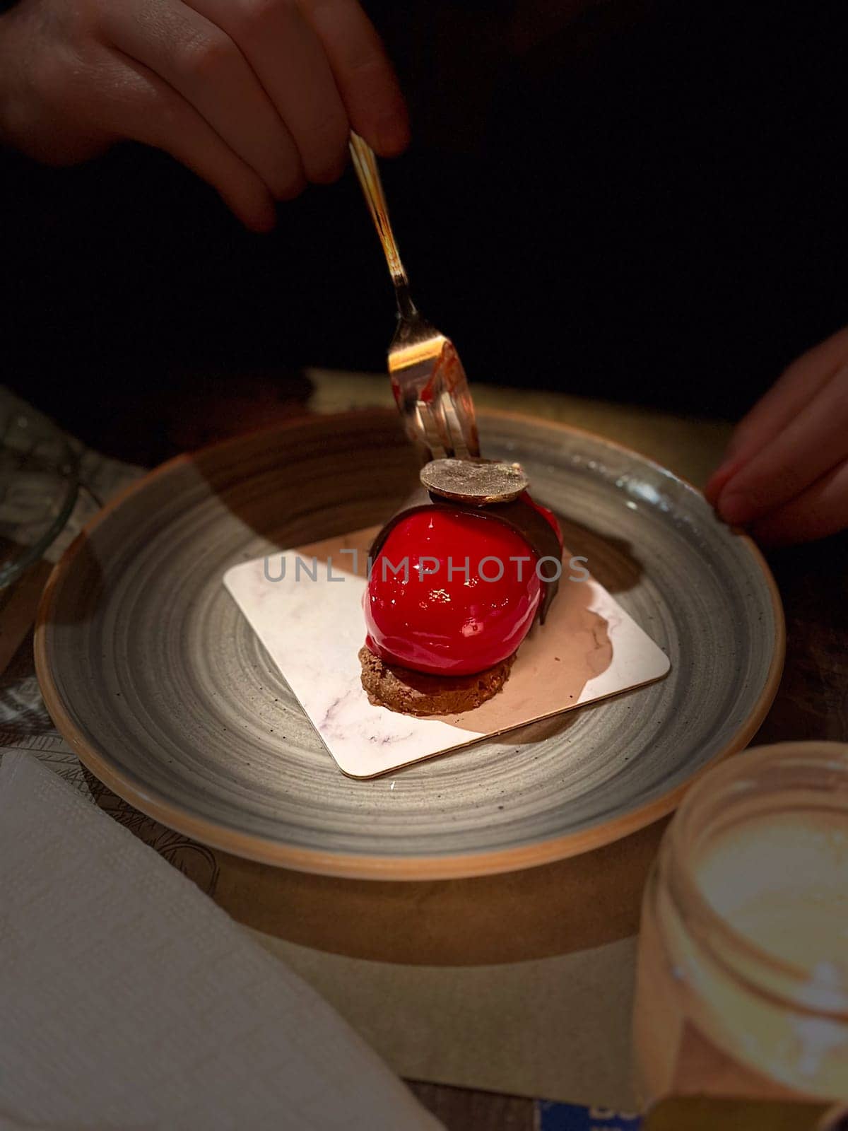 Close-up gourmet dessert with red glaze and chocolate decoration served on a plate, ready to be enjoyed in a cozy restaurant.