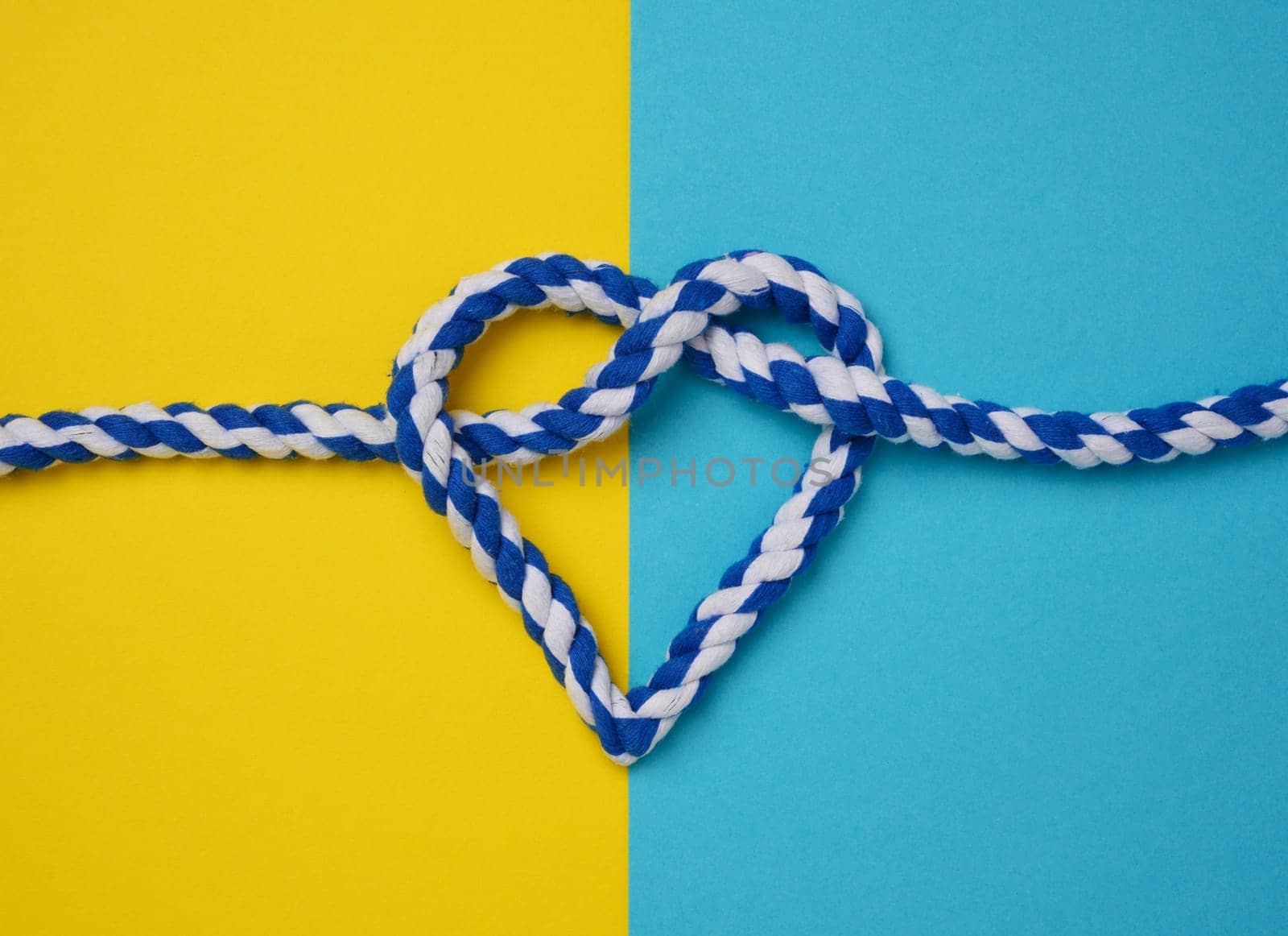 Thick blue rope tied in a heart shaped knot on a yellow background