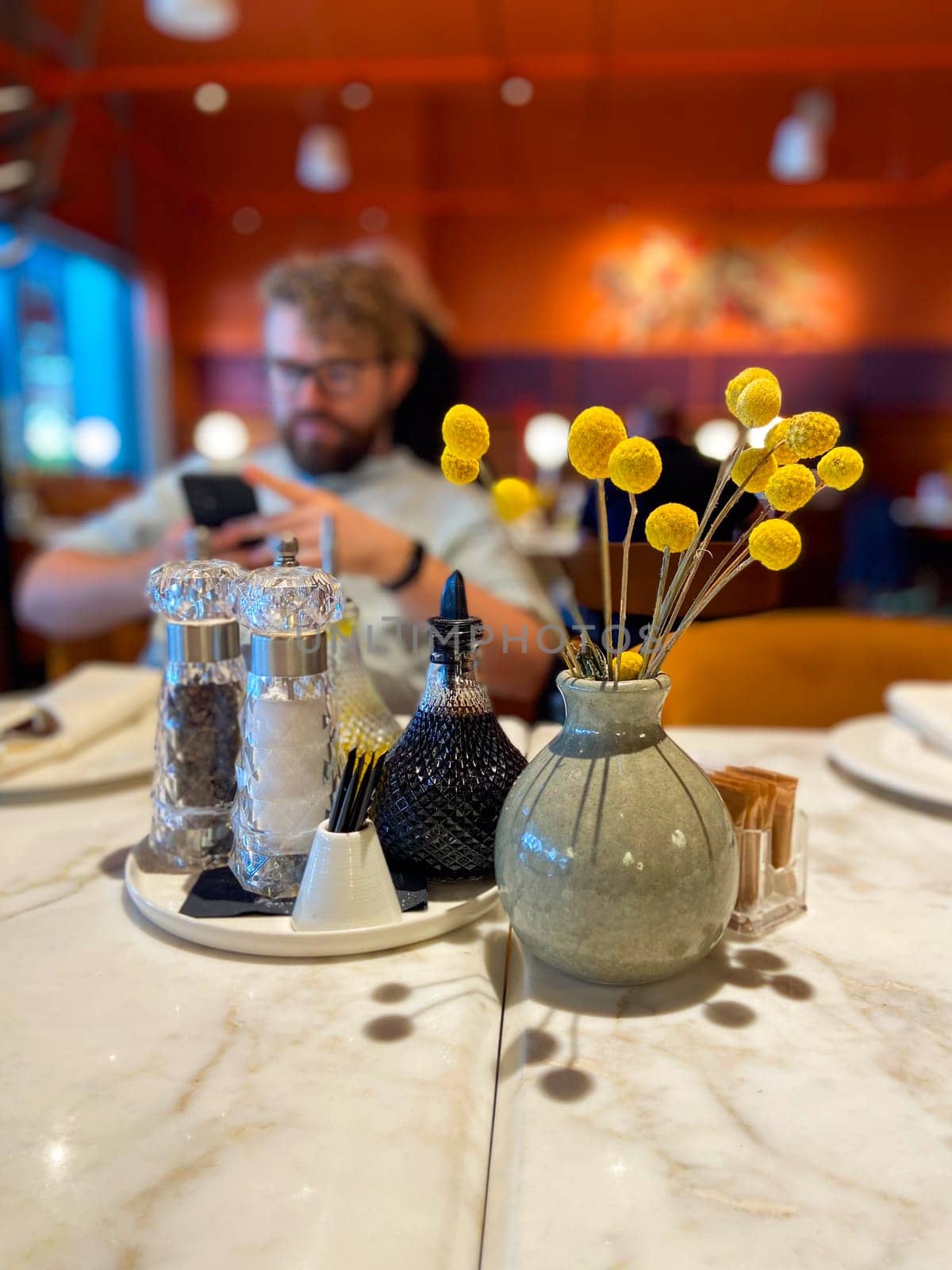 Table with decorative vase and condiment set in cozy restaurant ambiance. Warmth and elegance of a dining table setting, highlighting the intricate details of the decorations.
