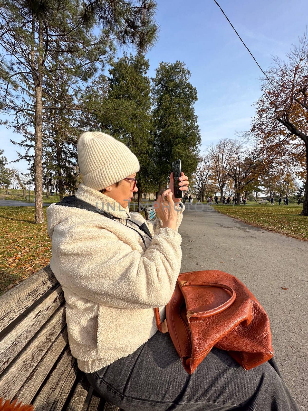 Woman taking a photo in a park on a sunny autumn day, moments of leisure and connection with nature amidst fall cold scenery.