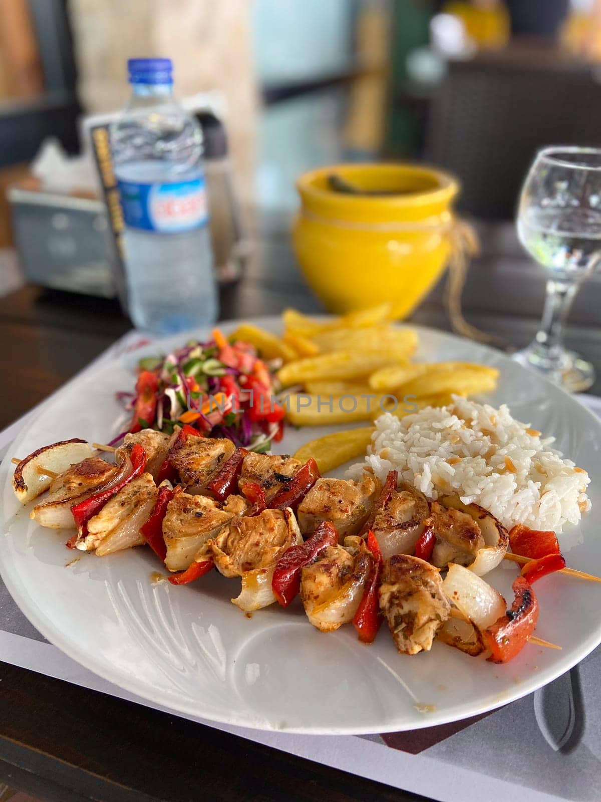 Delicious plate of grilled chicken skewers with rice, salad, and fries on a wooden table setting. Well-balanced and colorful meal, perfect for a vibrant dining experience.
