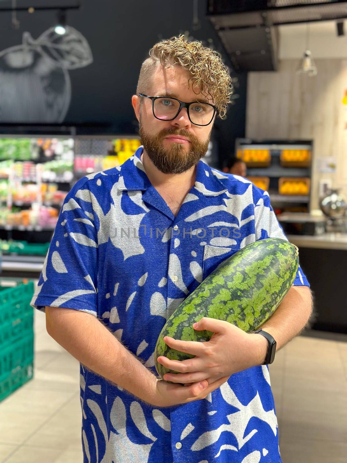 Millennial man holding a watermelon in a grocery store. Moment of everyday life with a vibrant display of produce and personal style.