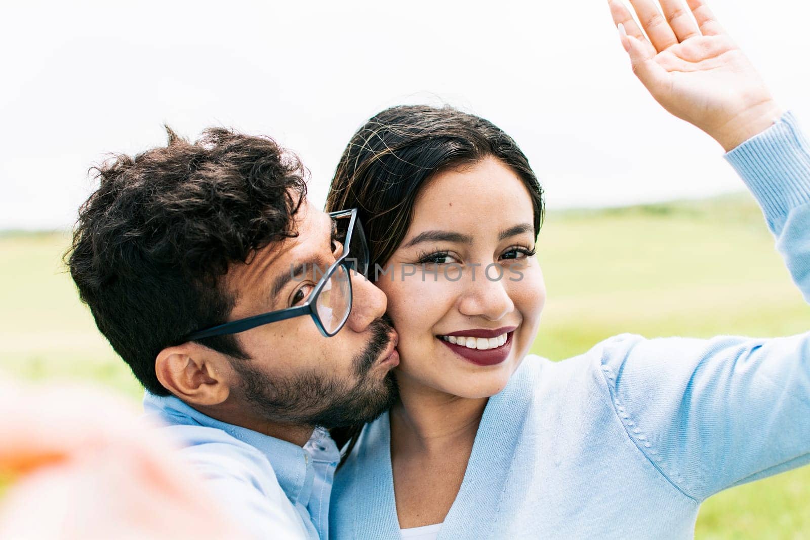 Selfie of young happy couple kissing in the field. Cute couple in love taking a selfie in the field, looking at the camera