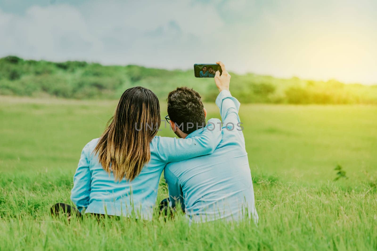 Couple in love taking a selfie sitting in a beautiful field. Young happy couple taking a selfie sitting in the field