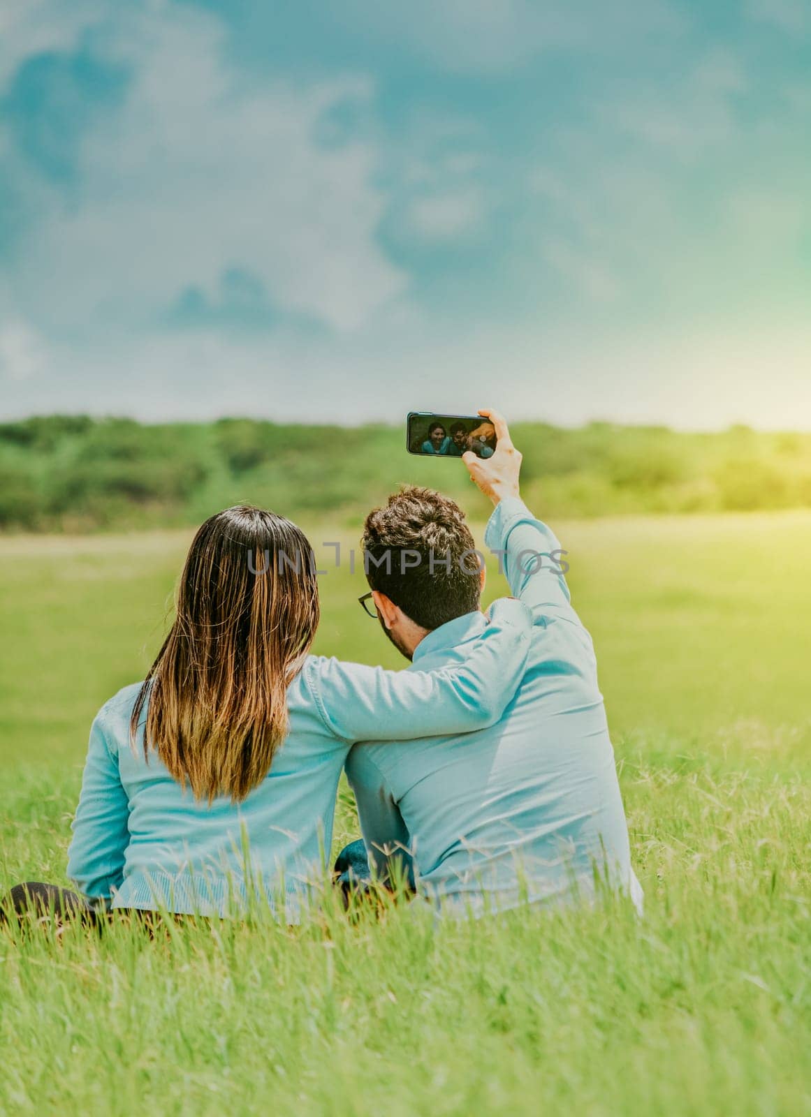 Young happy couple taking a selfie sitting in the field. Couple in love taking a selfie sitting in a beautiful field