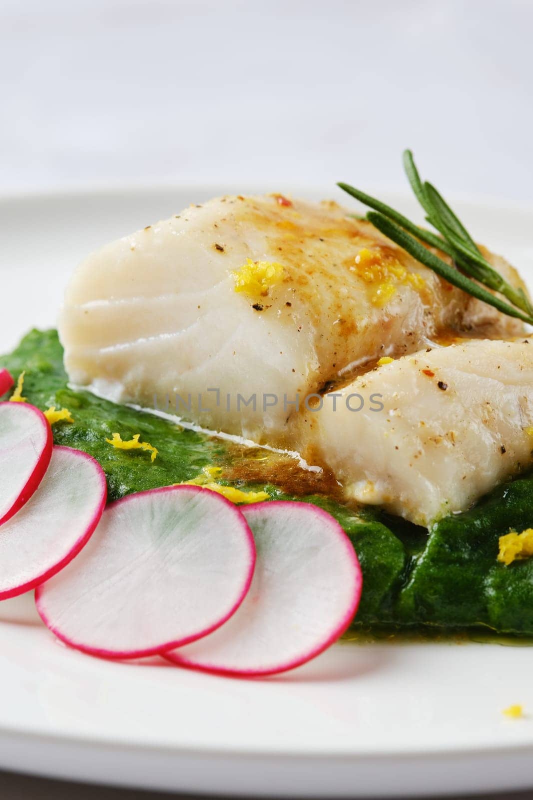 A tender white fish fillet is elegantly placed atop vibrant wilted greens. Fresh radish slices and citrus zest add a burst of color and flavor, creating a refined culinary presentation.