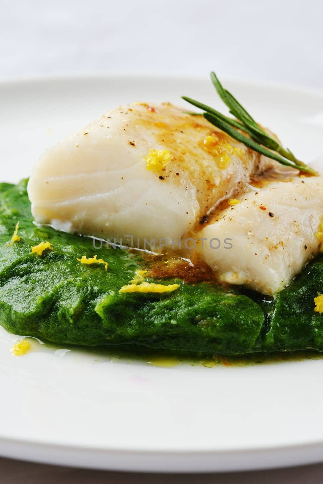 A succulent cod fillet sits atop a beautiful green spinach puree, garnished with herbs and citrus zest. The dish showcases a harmonious blend of flavors in a simple yet elegant presentation.