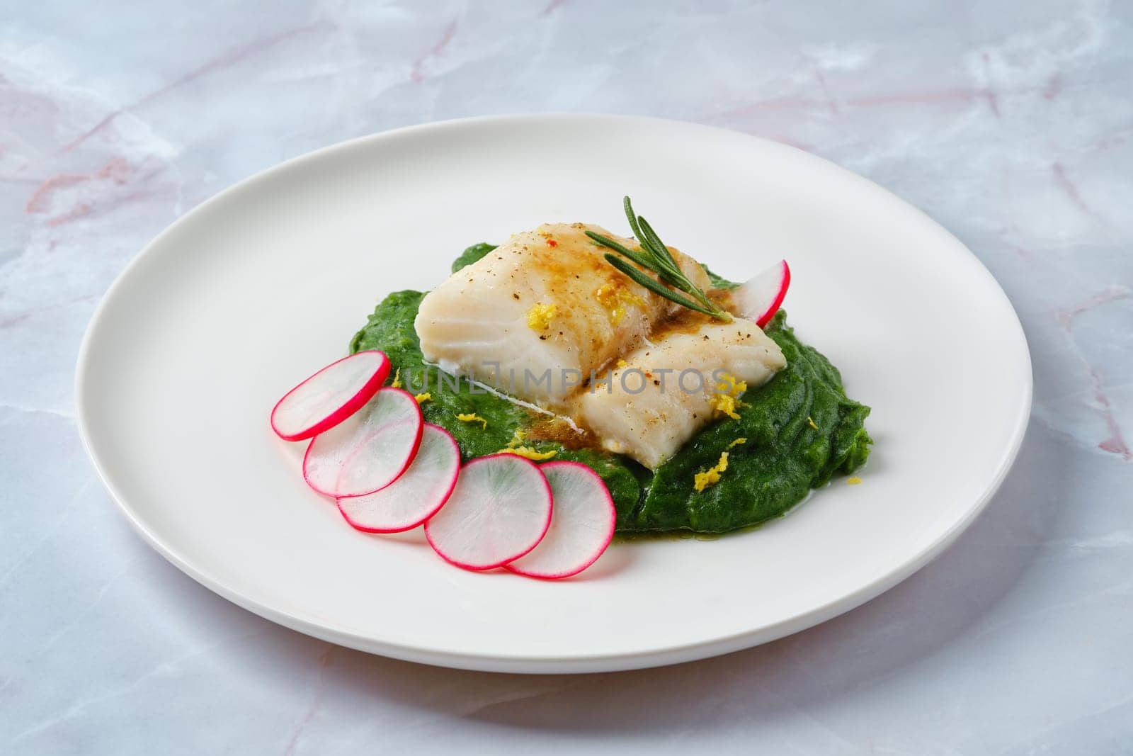 A beautiful presentation of a fish fillet garnished with herbs lies atop a smooth spinach puree, complemented by thin slices of radish for a touch of freshness and color, making it an enticing dish.