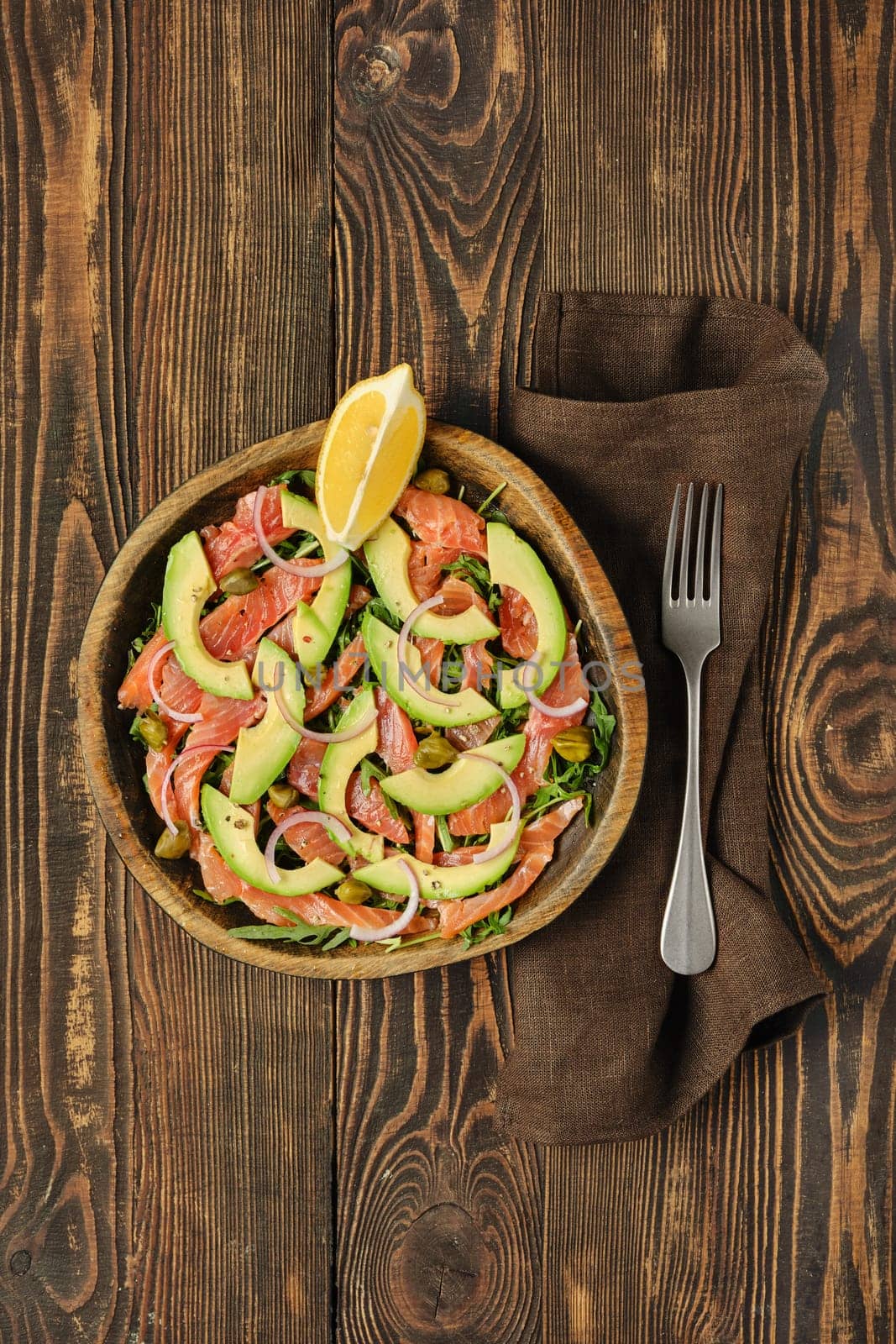 Overhead view of salad with fresh salmon, avocado and onion served in a wooden bowl on a rustic wooden table