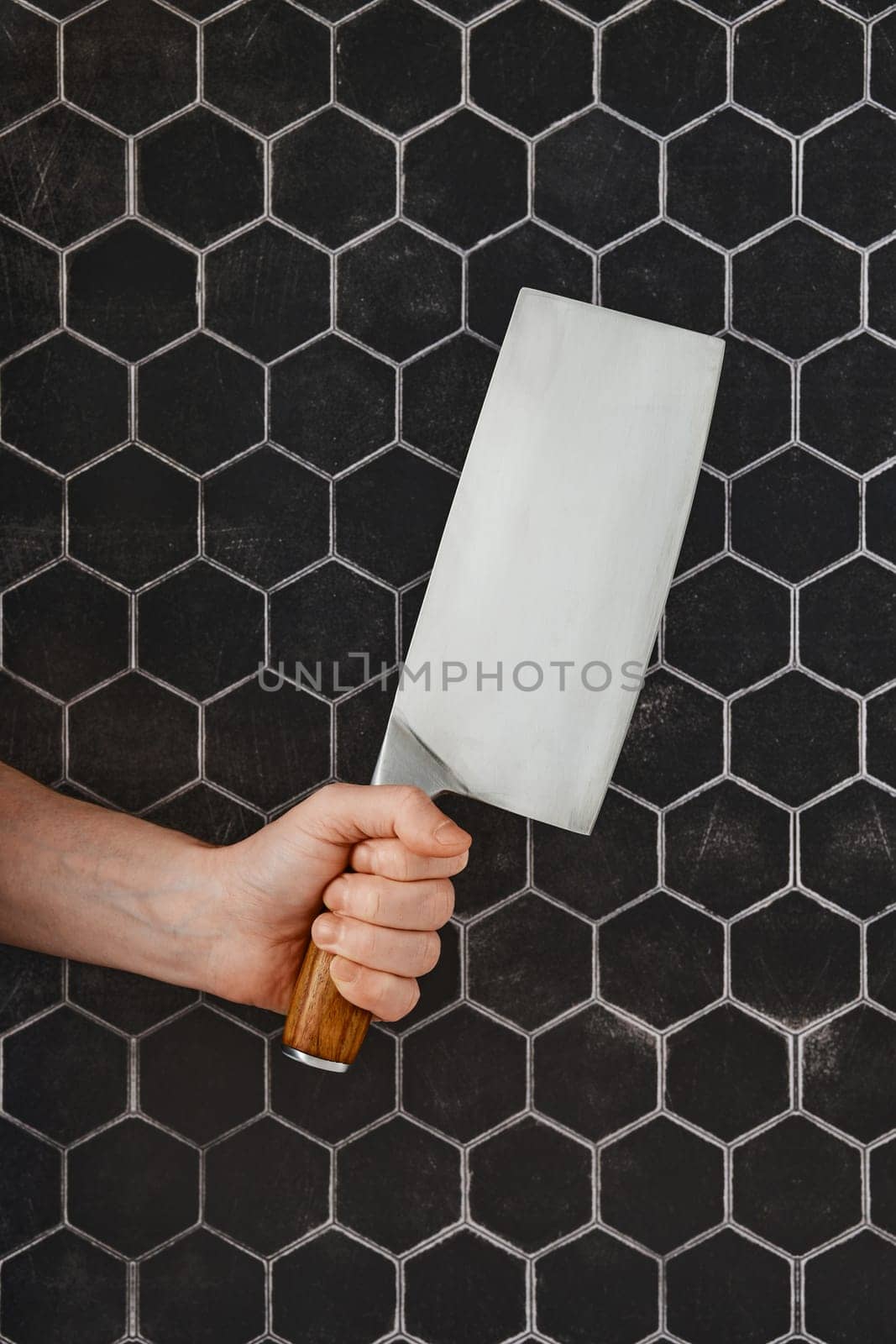A hand grips a large kitchen cleaver, positioned against a striking hexagonal tile backdrop. The wooden handle adds a touch of warmth to the contemporary kitchen environment.