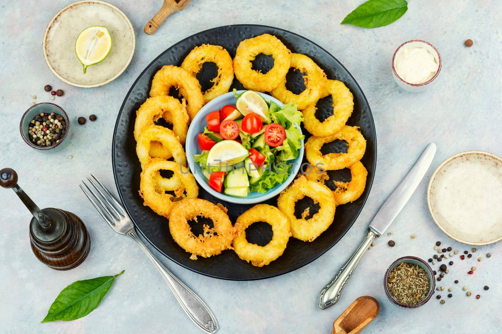 Serving of calamari, deep-fried squid rings, garnished with vegetable salad. Close up.