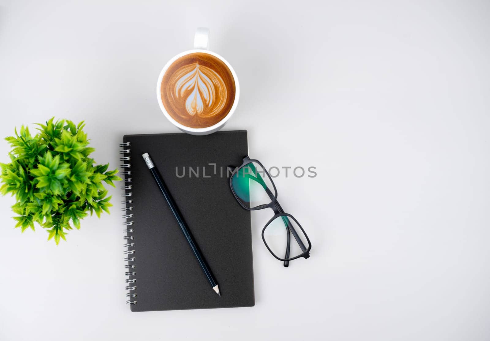 Top view white workspace office desk with office supplies. Flat lay work table with black notebook, Green leaf and coffee cup, Copy space for your advertising content.