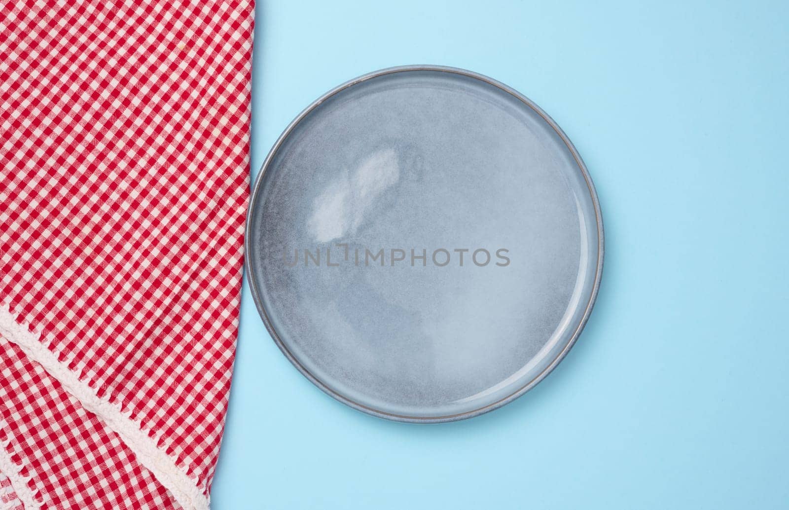 Round ceramic empty blue plate and red kitchen towel, top view