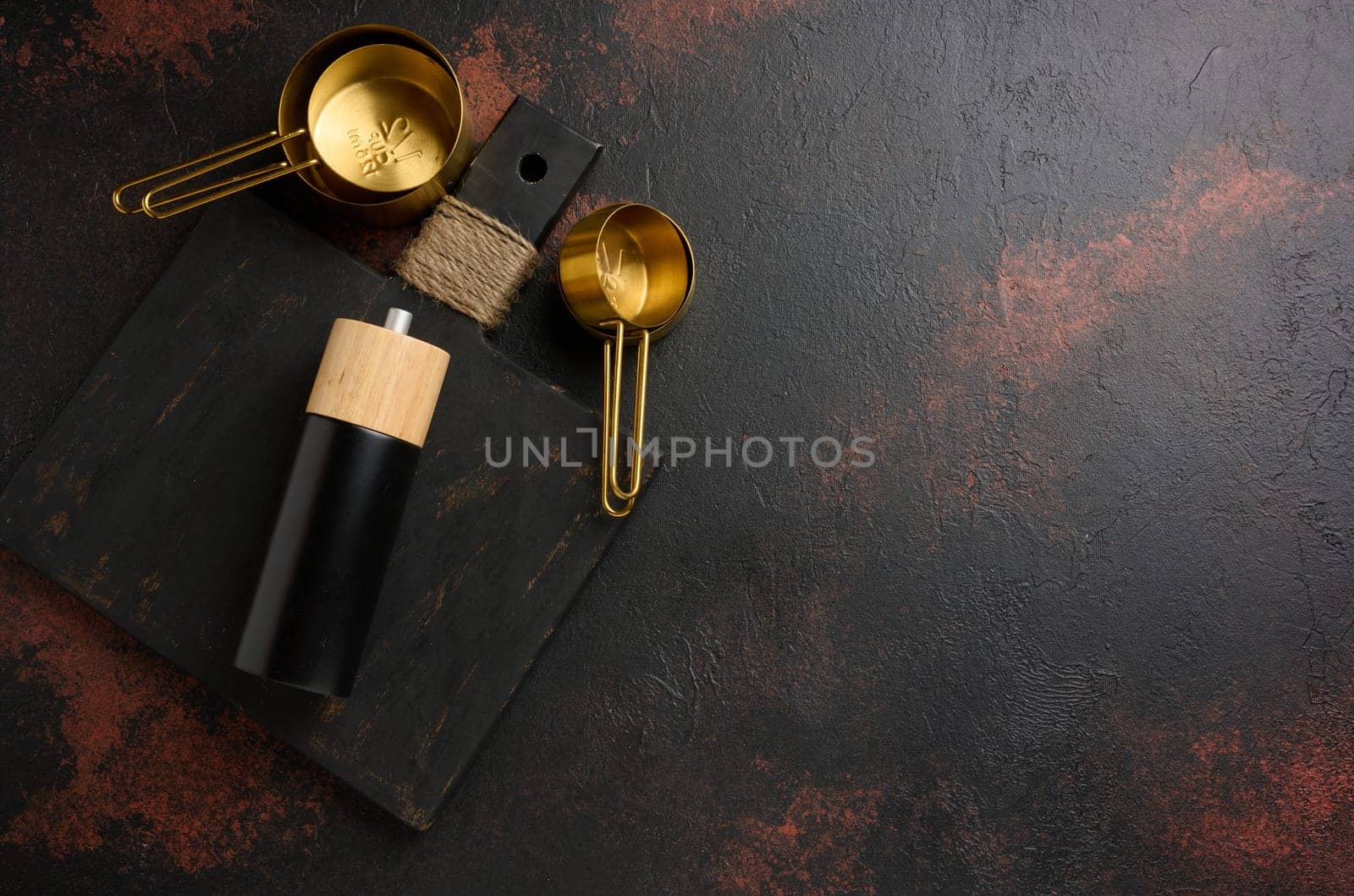 Wooden kitchen cutting board, kitchen utensils and pepper mill on black counter, top view