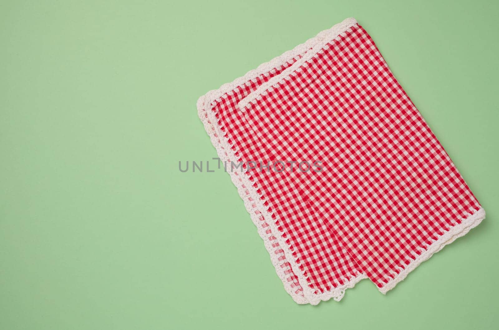 Folded red kitchen towel on a green background, top view.