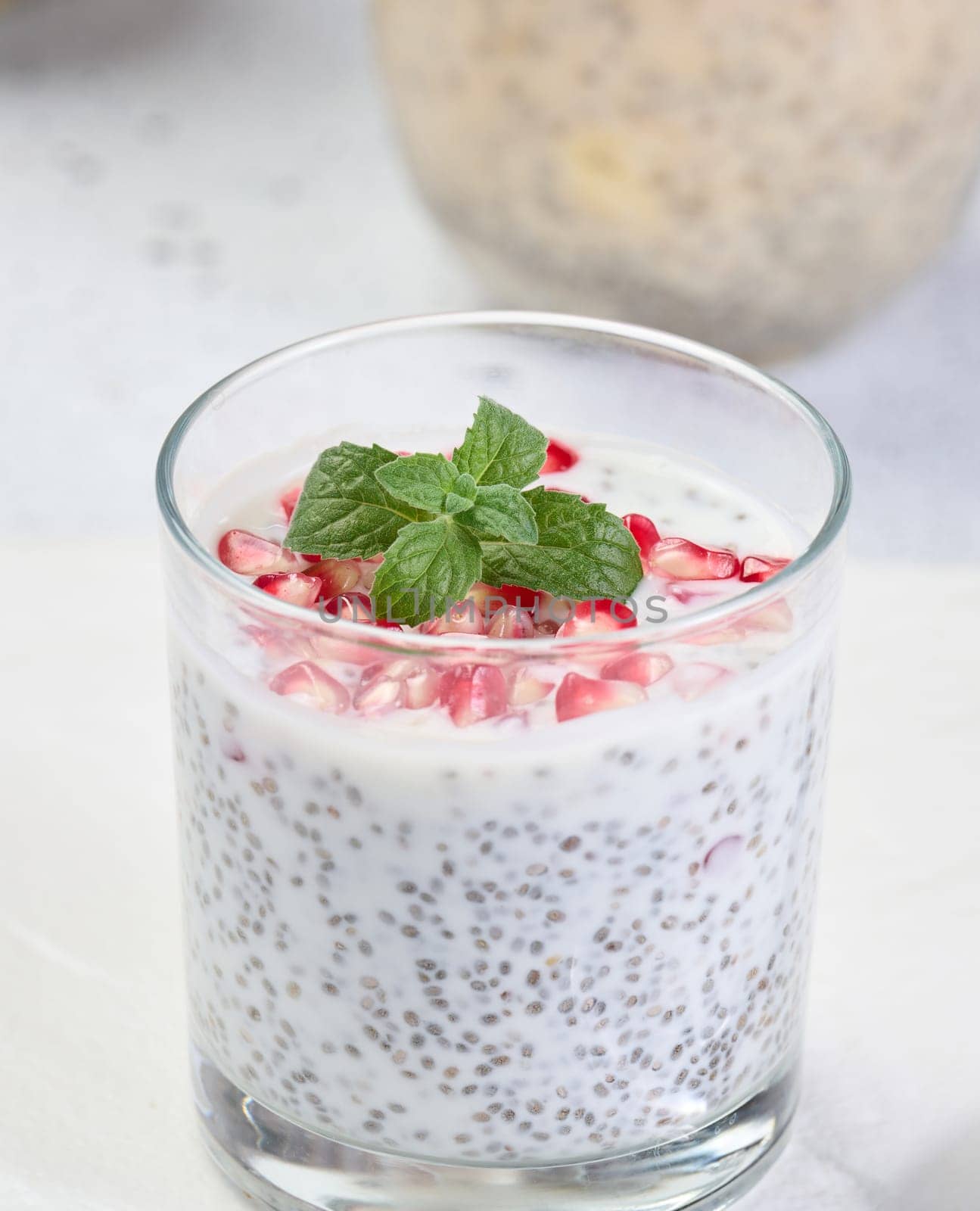 Glass with chia and yogurt dessert decorated with fresh fruits and pomegranate seeds on white table