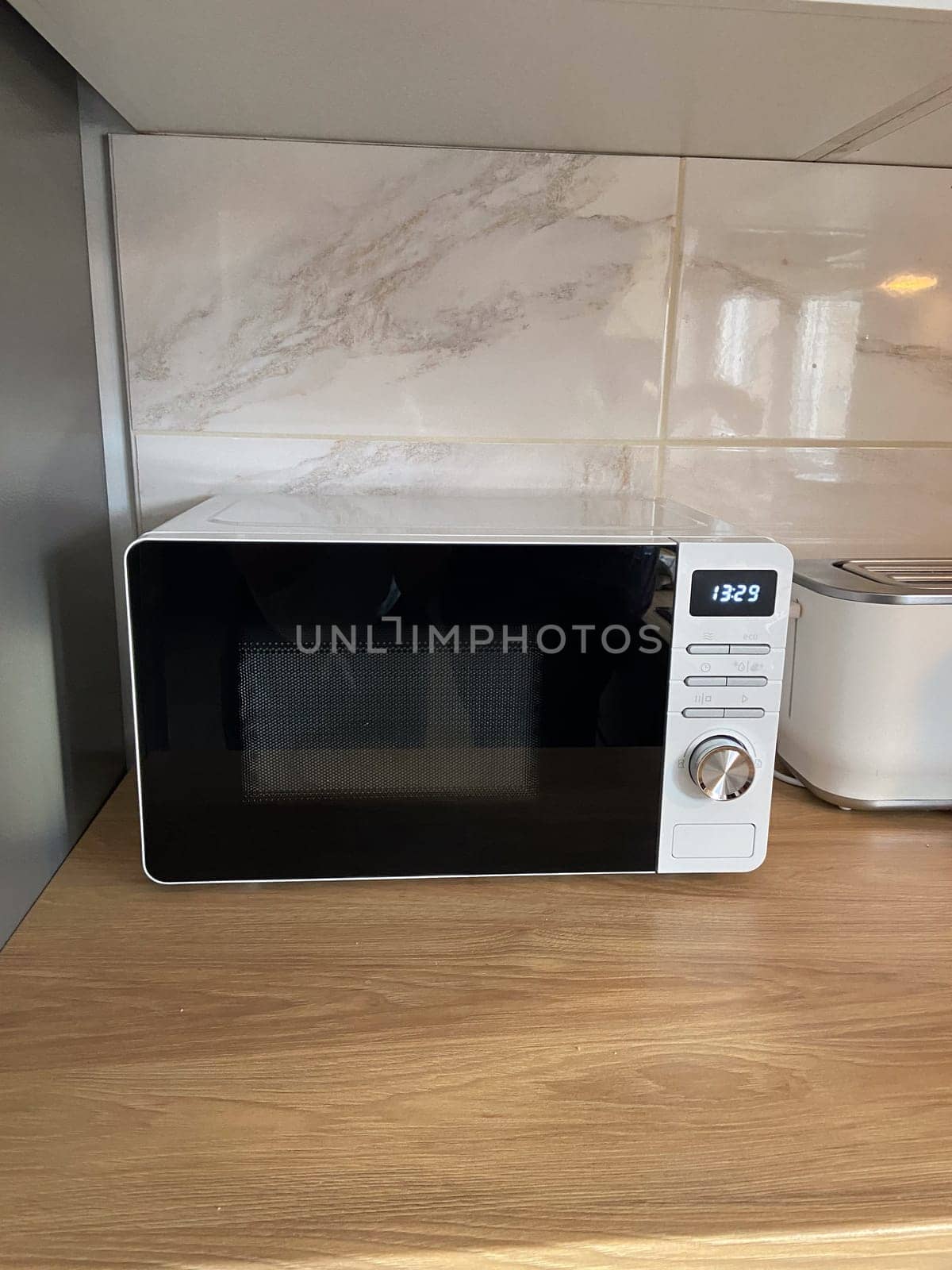 Modern kitchen corner features a microwave, a toaster on a wood countertop. Minimalist design with sleek white cabinets and marble backsplash creates a clean and organized cooking space