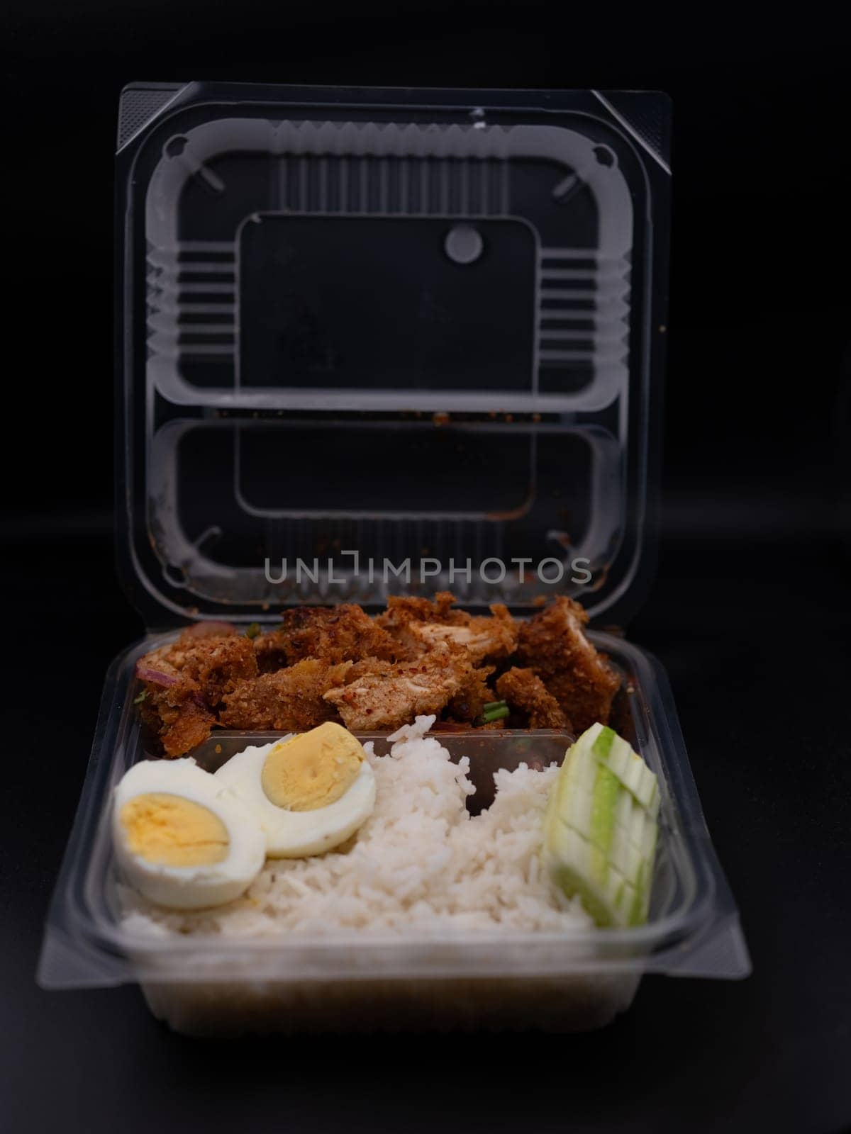 Spicy chicken rice salad with boiled eggs put in a clear plastic box.
