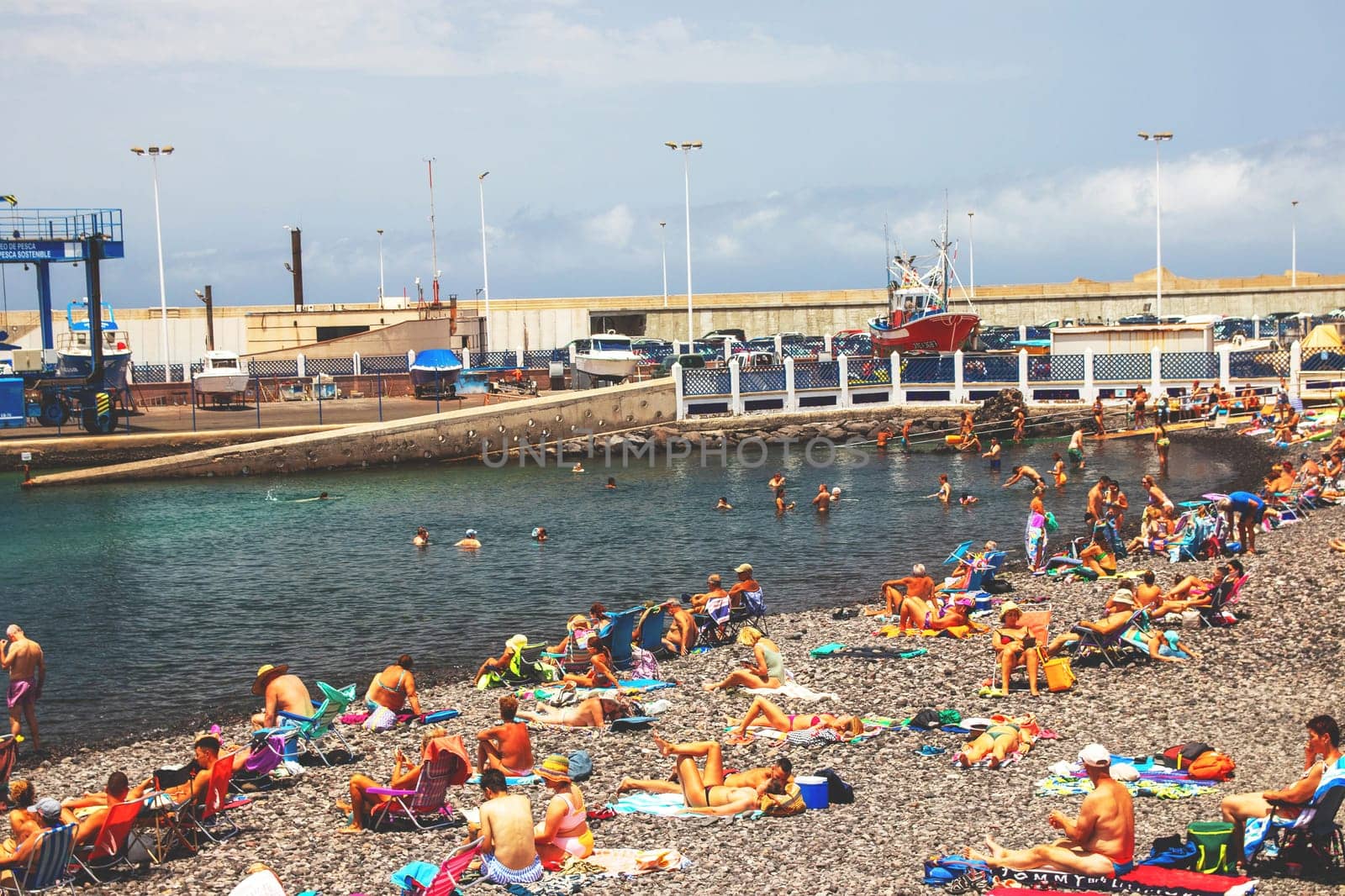 Puerto de las Nieves, Gran Canaria Island, Spain - 20 July 2024. tourists on the stony beach Playa de las Nieves with a view of the harbour.