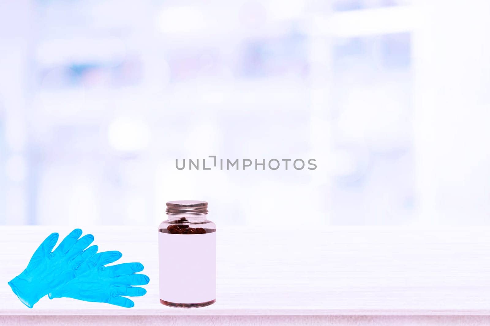 Closeup of a pair of blue medical doctor gloves or surgical gloves and a glass bottle medicine with empty label on table over abstract blurred hospital background. Space.