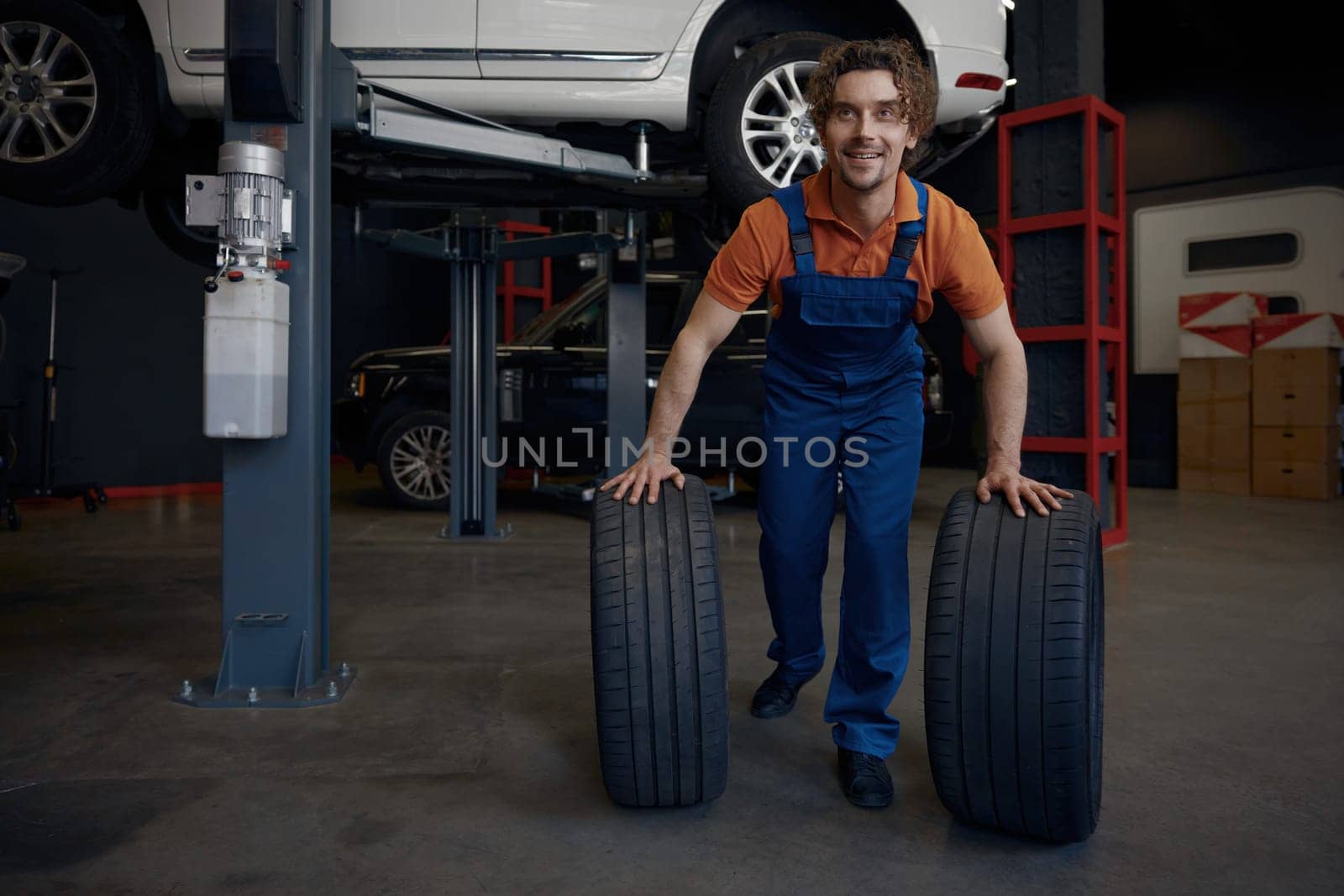 Repairman rolling car spare tires while working on wheel replacement providing professional automotive mechanical