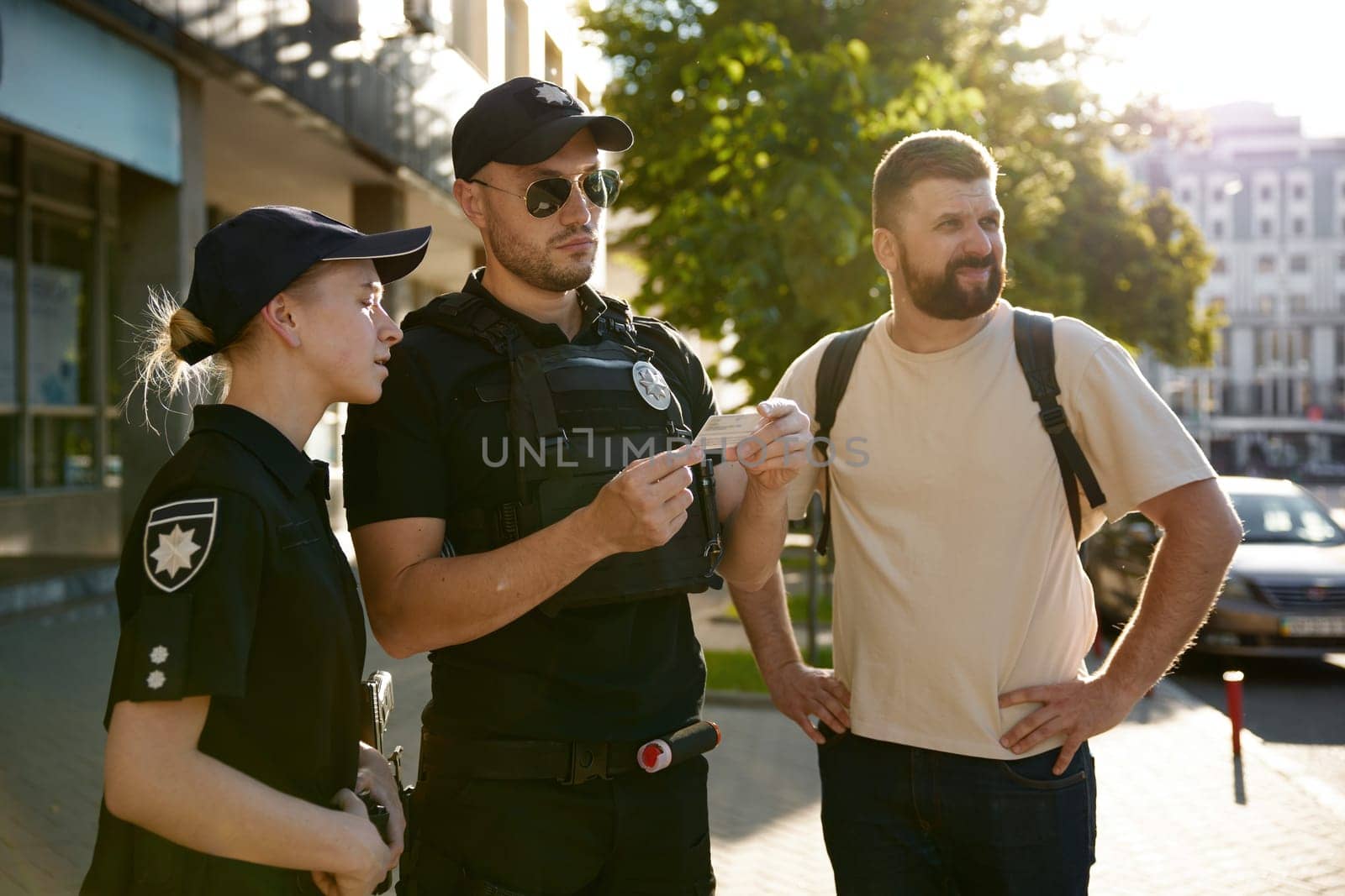 Serious patrol policeman and policewoman checking personal documents of citizen on city street