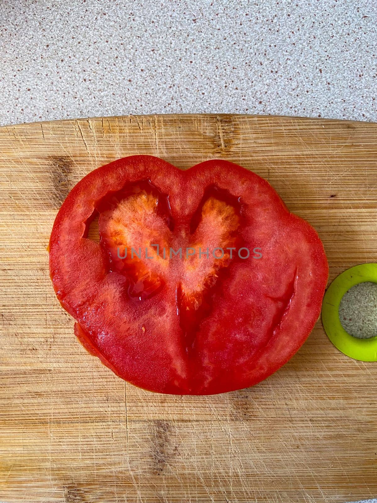 Vibrant tomato slice reveals a heart shaped pattern, resting on a wooden cutting board. Freshness of tomato adds a touch of nature artistry to a simple kitchen moment. Valentine day.
