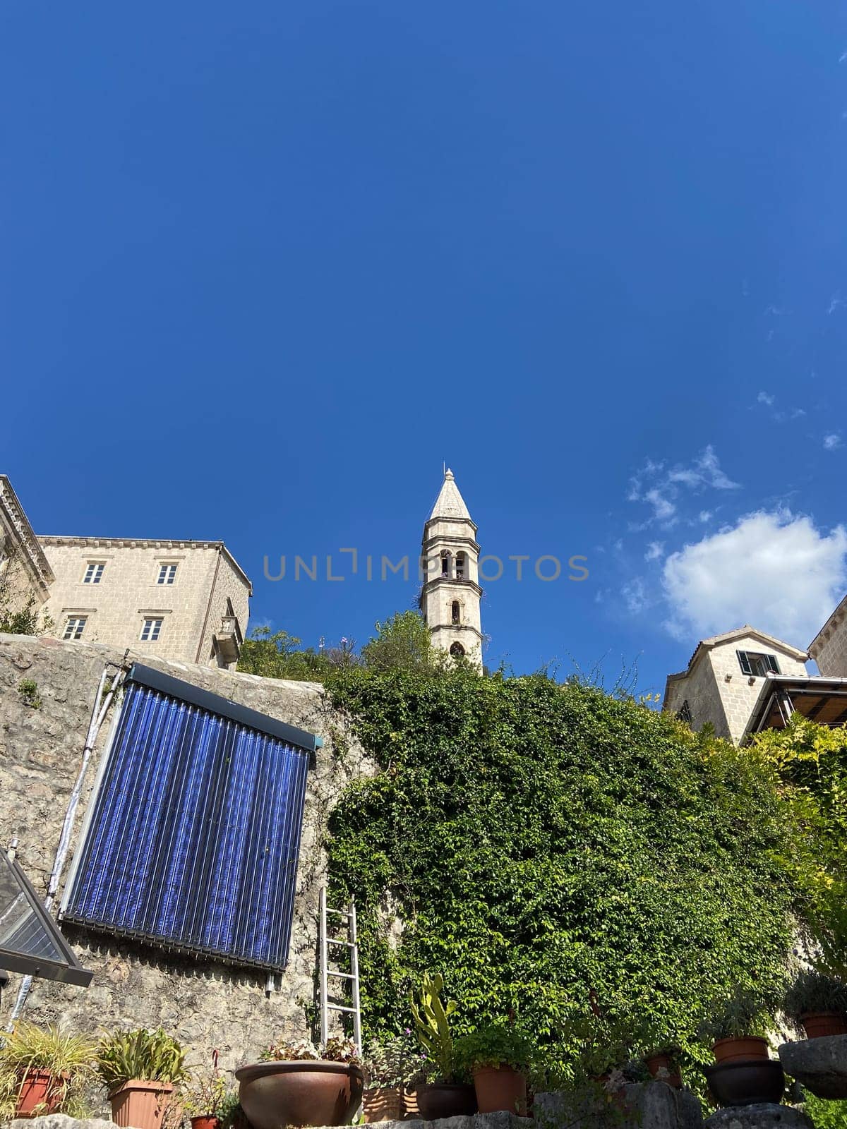 Historic church tower rises above charming, ivy-covered stone wall under a vibrant blue sky. Scene captures essence of timeless architecture and natural beauty in a quaint village setting.