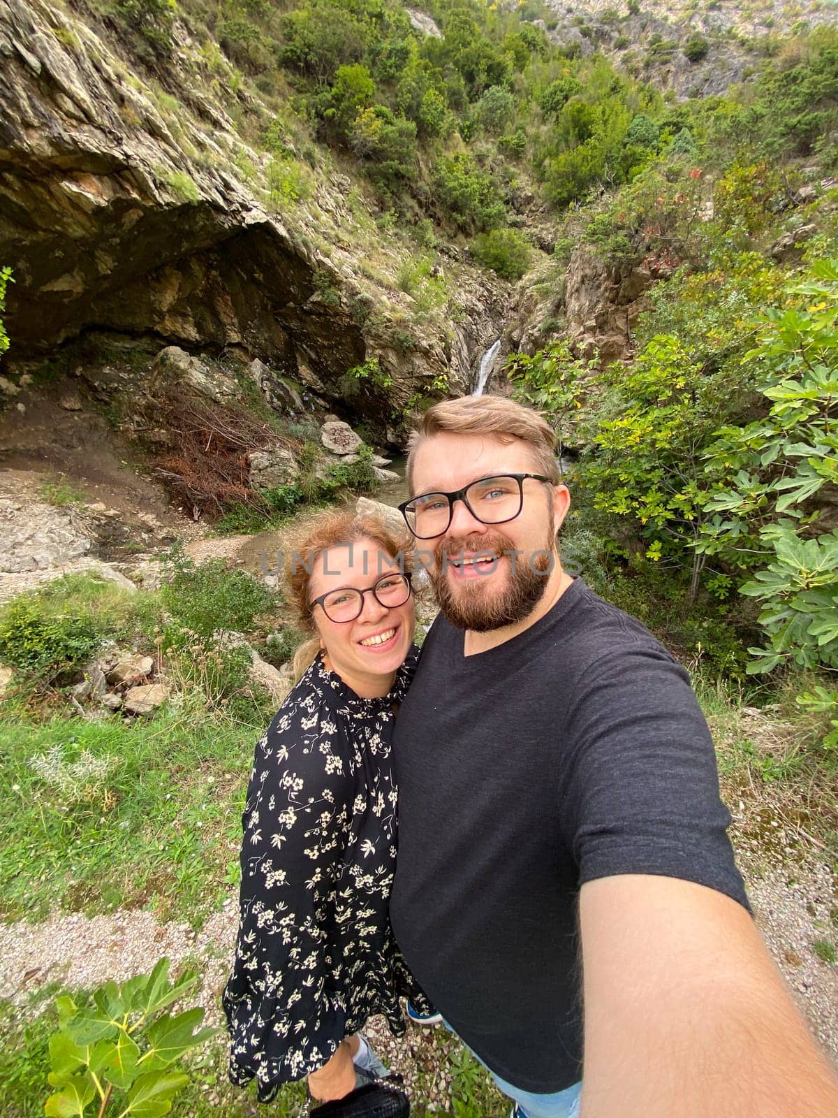 Millennial joyful couple takes a selfie in a lush, mountainous landscape, celebrating their outdoor adventure. Beauty of nature and the happiness of shared experiences.