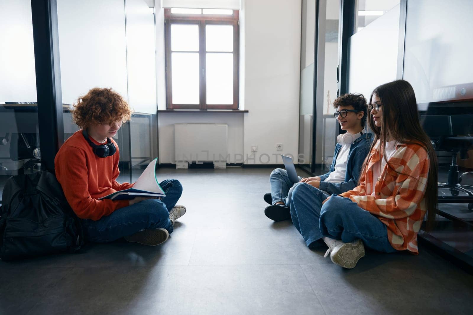 Some teenagers sitting on floor in office. Group of young smart workers having a fun conversation together, enjoying teamwork