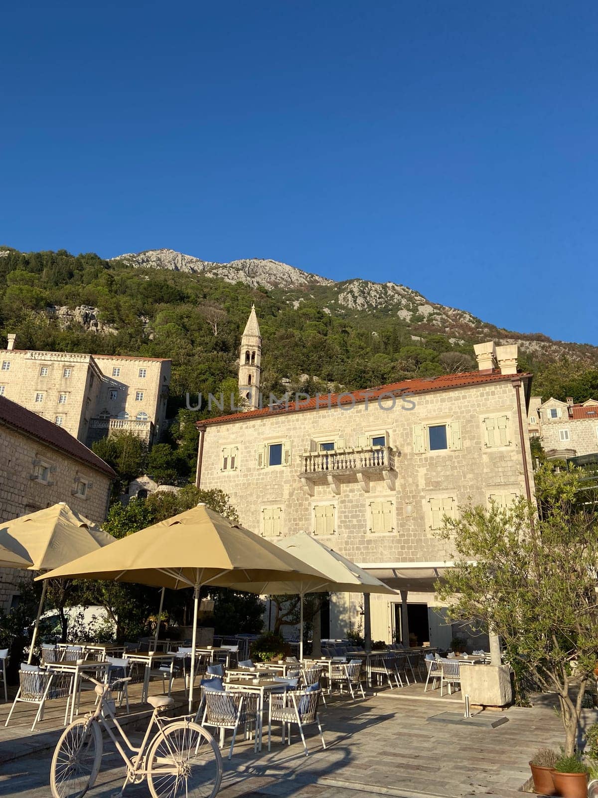 Outdoor cafe in a historic stone building nestled at base of green mountain under a clear blue sky. Tranquil blend of architecture and nature, perfect for a relaxed afternoon