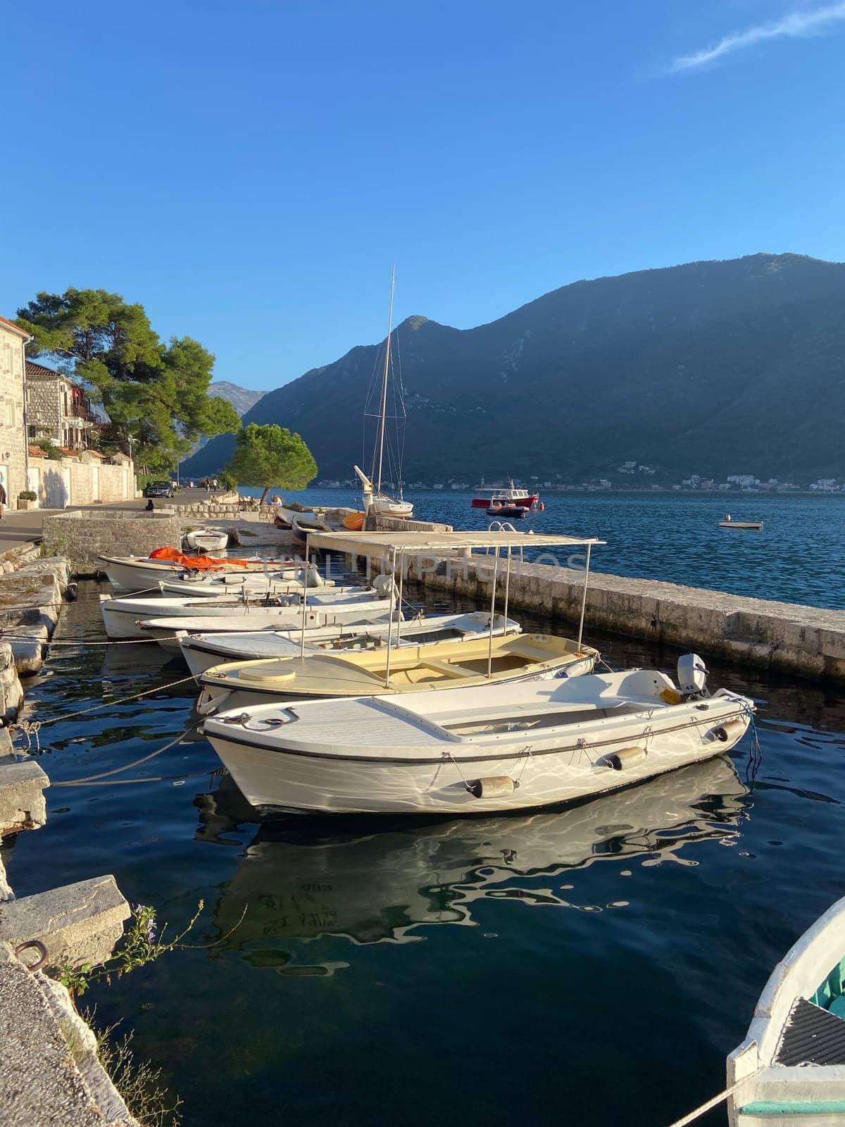 Small wooden boat floats calmly in a serene harbor, tied to dock as gentle waves reflect surrounding landscape. Coastal life and tranquil maritime environments.