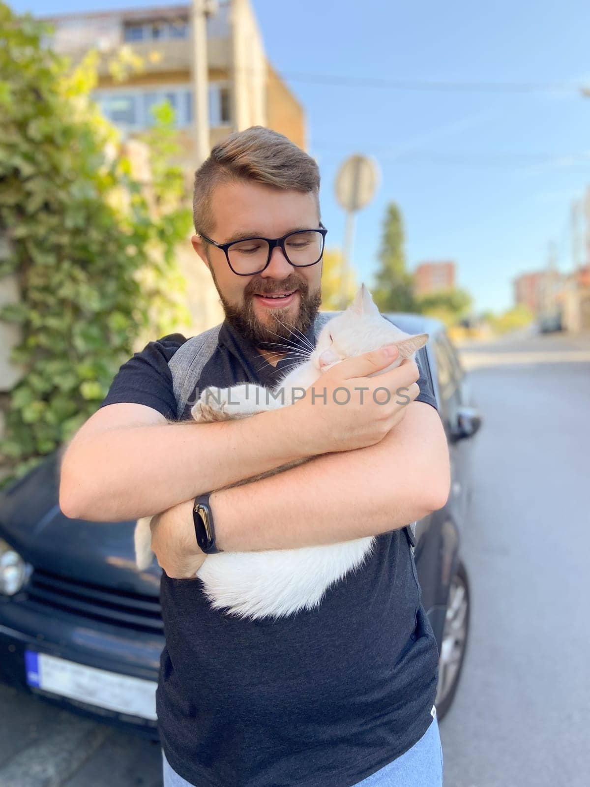 Bearded man gently embraces a white cat, conveying a moment of warmth and connection with pet. Outdoor setting adds an element of everyday life and companionship.