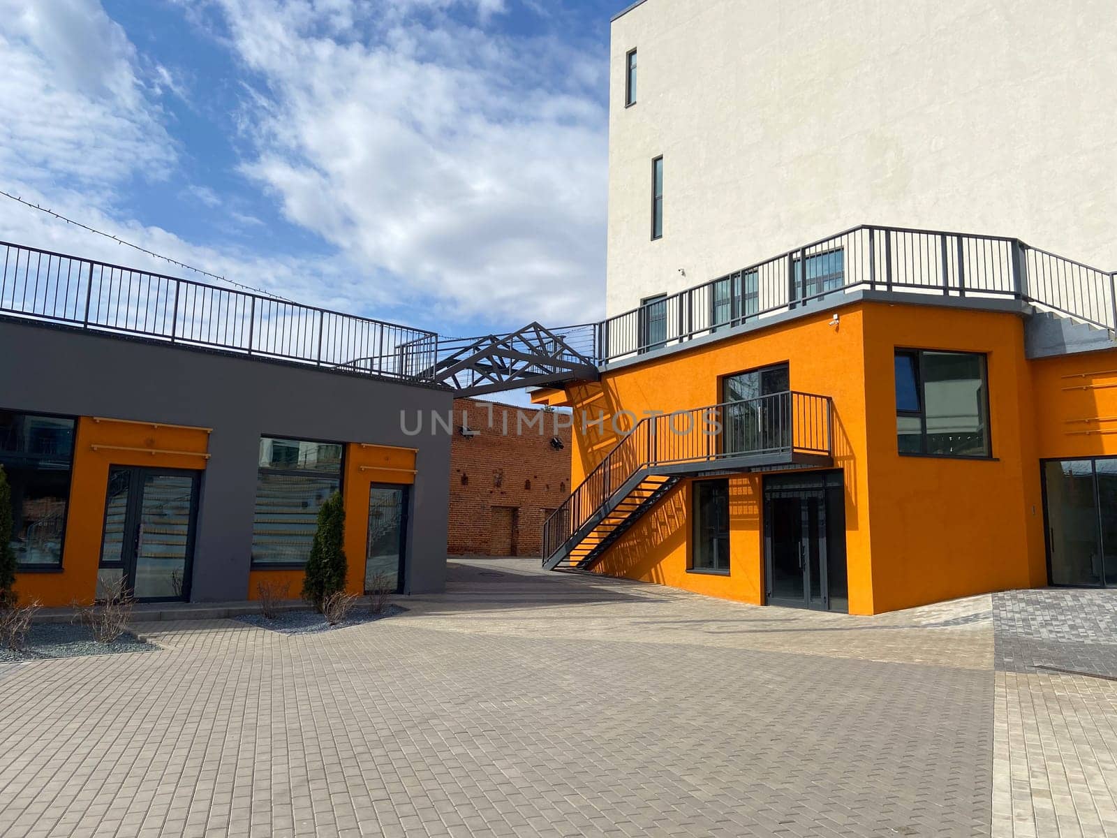 A contemporary street view showcasing orange building, large windows, and sidewalk with wooden benches, in autumn season.
