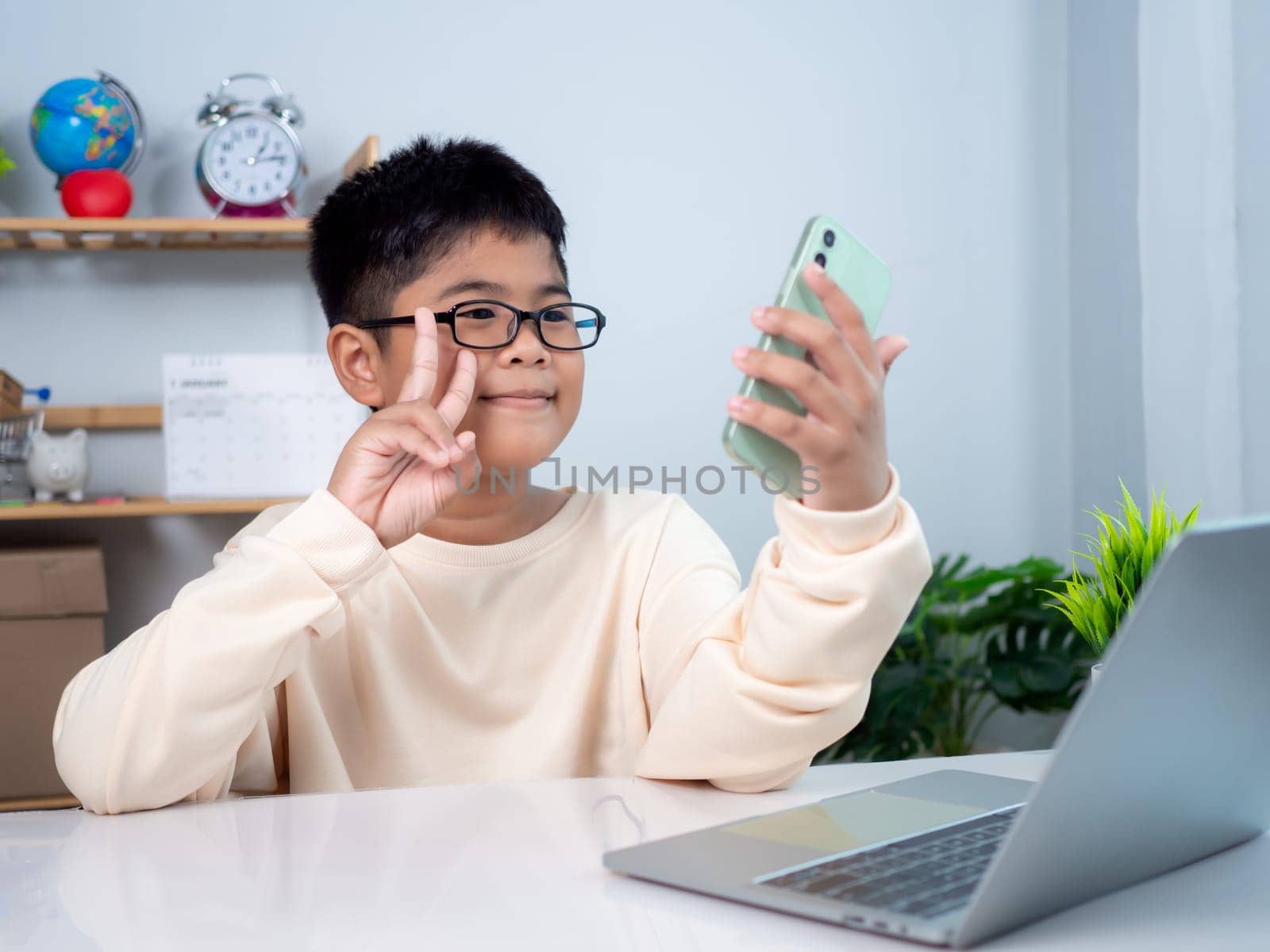 Asian student boy using computer and phone learning. Educational of tech concept, Staying at home, Presenting a modern educational way of life. Virtual internet online class from school teacher.