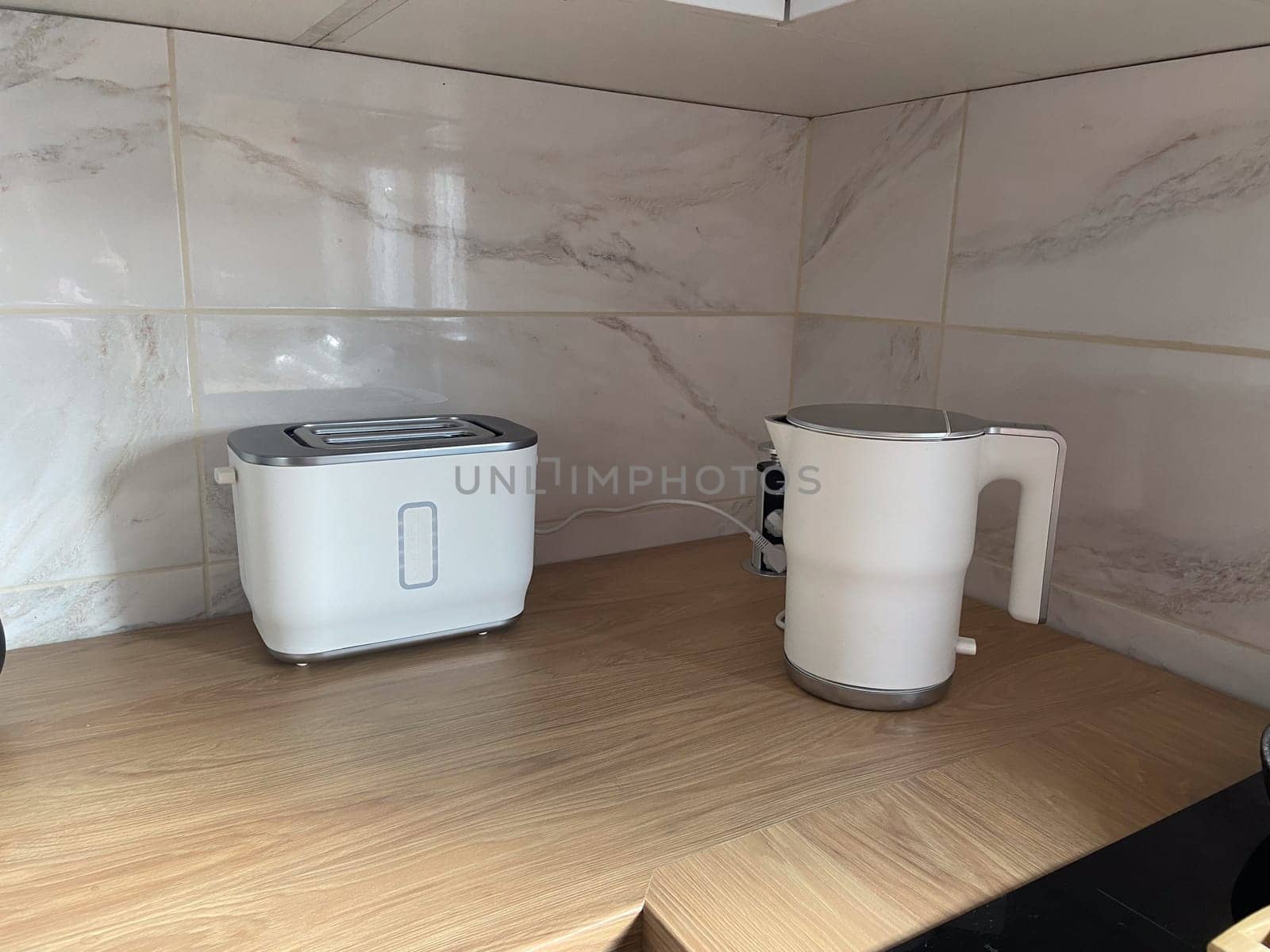 Modern kitchen nook featuring a sleek toaster and electric kettle on a wooden countertop. Minimalist design and clean lines create a functional and stylish space.