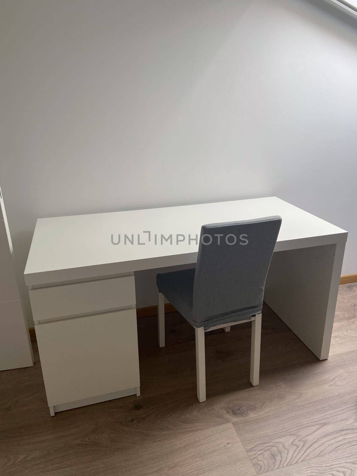 Minimalist workspace with a white desk and a gray chair on a wooden floor. Simple design offers a clean and organized environment perfect for productivity and focus.