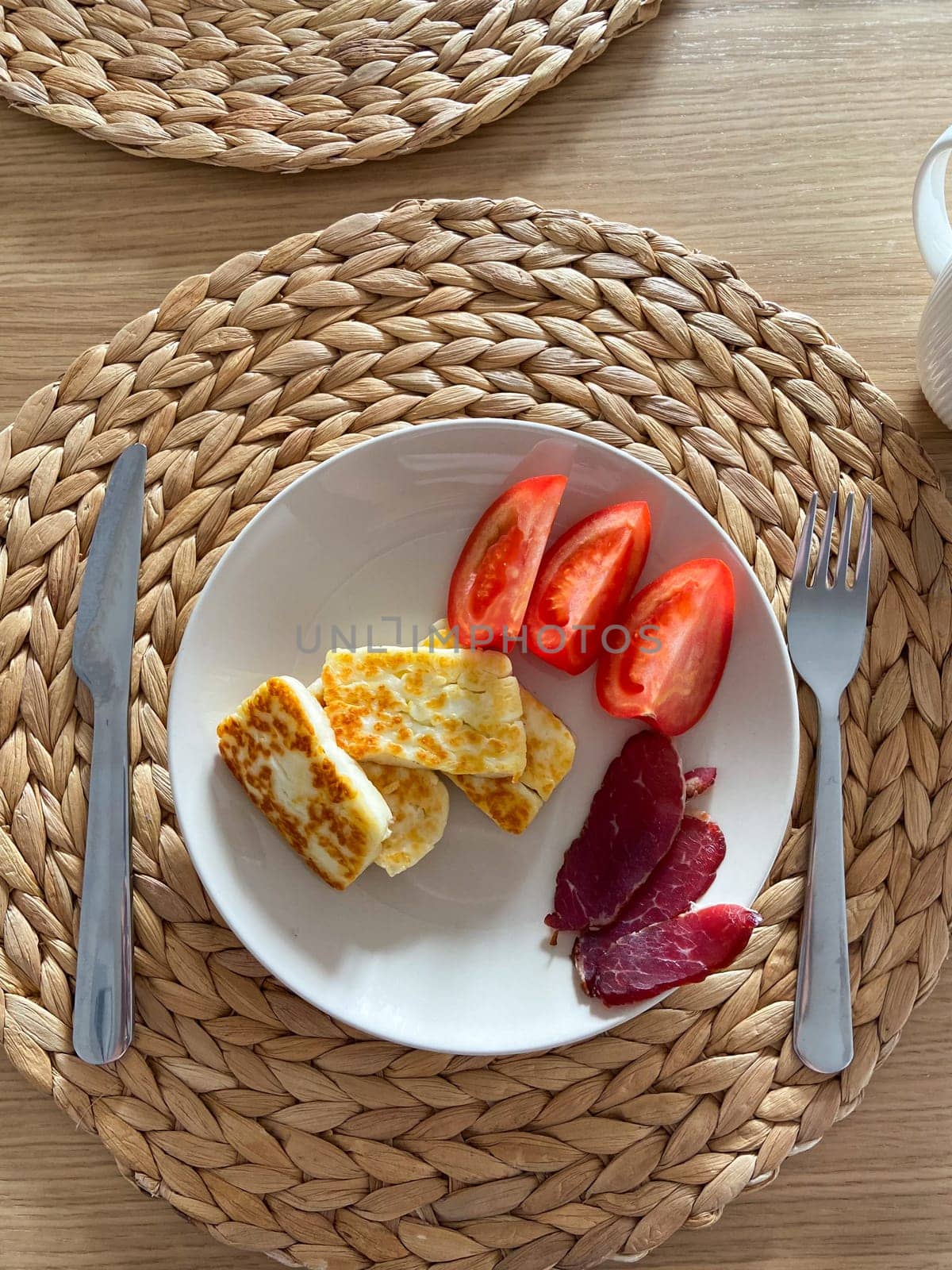 Cozy breakfast setting features plates with cheese, tomatoes, and cured meat. Woven placemats and wooden table provide a warm, inviting ambiance.