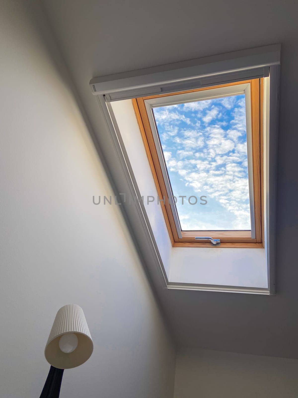 Clear sky view through a skylight reveals a vibrant array of clouds, offering a serene glimpse of outdoors. Wooden frame adds warmth and contrast to the bright blue sky.