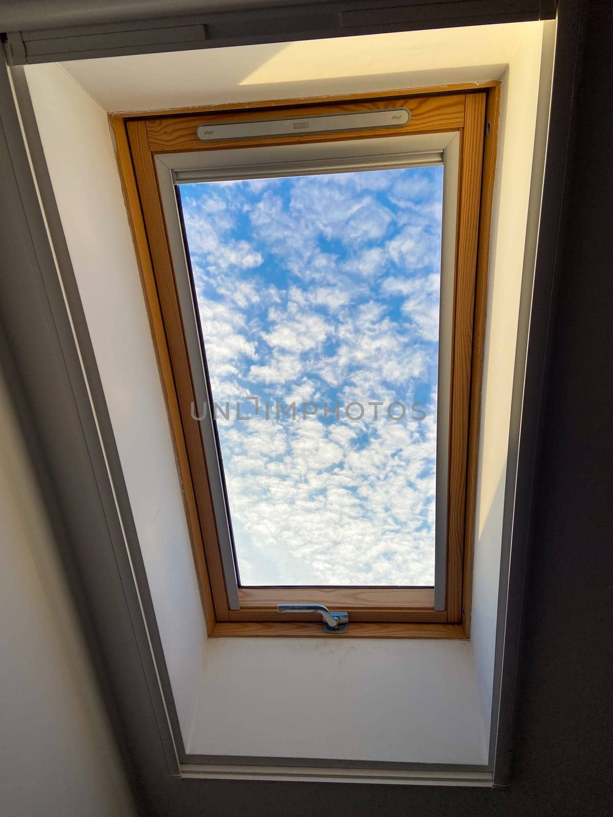 Clear sky view through a skylight reveals a vibrant array of clouds, offering a serene glimpse of outdoors. Wooden frame adds warmth and contrast to the bright blue sky.