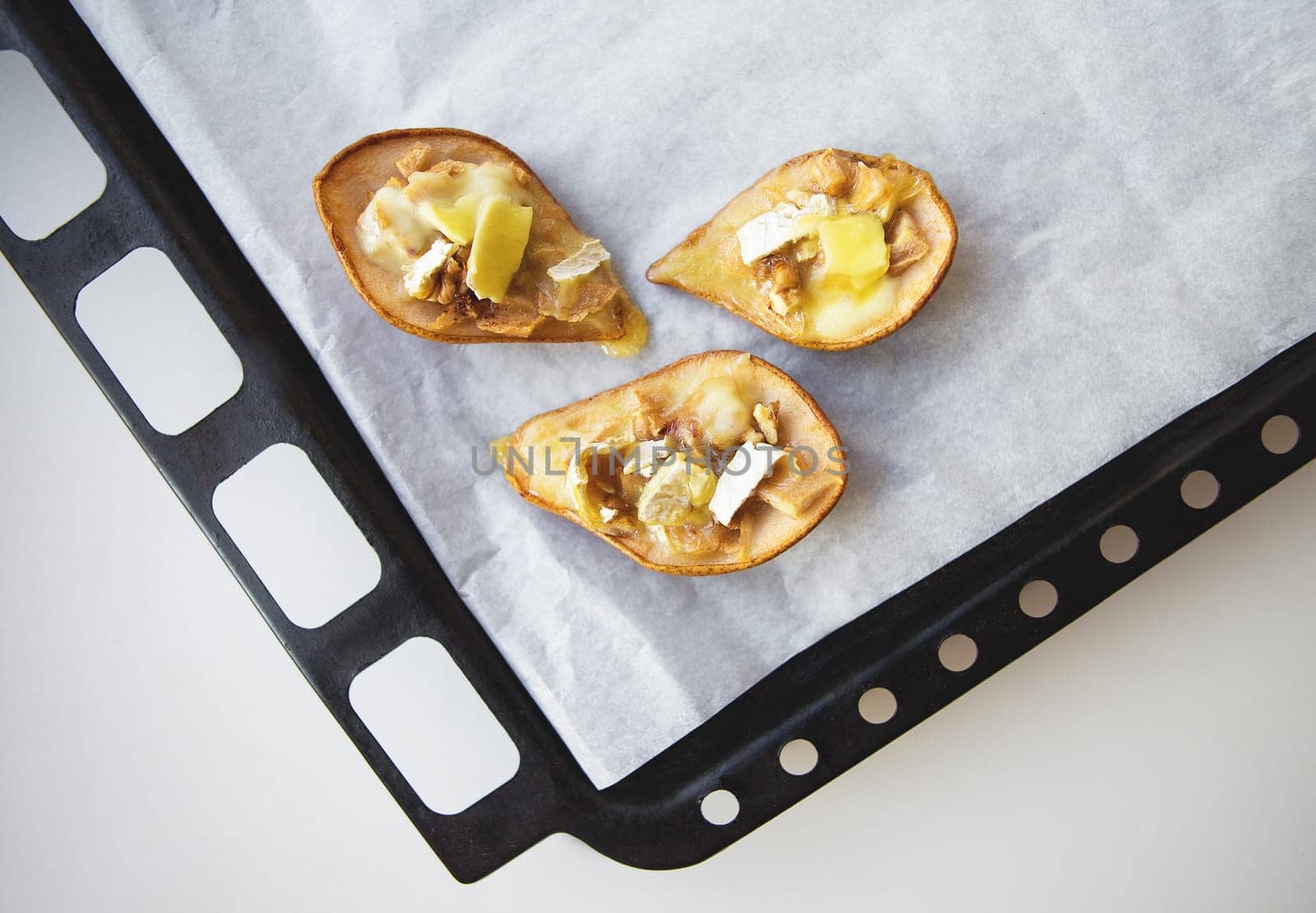 juicy pear baked with cheese and nuts lying on a baking sheet.