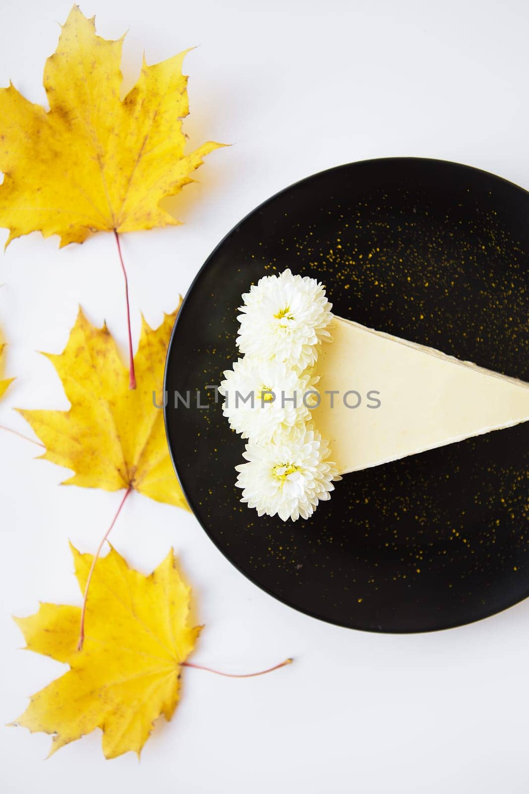 creamy cheesecake on a black plate decorated with yellow maple leaves.