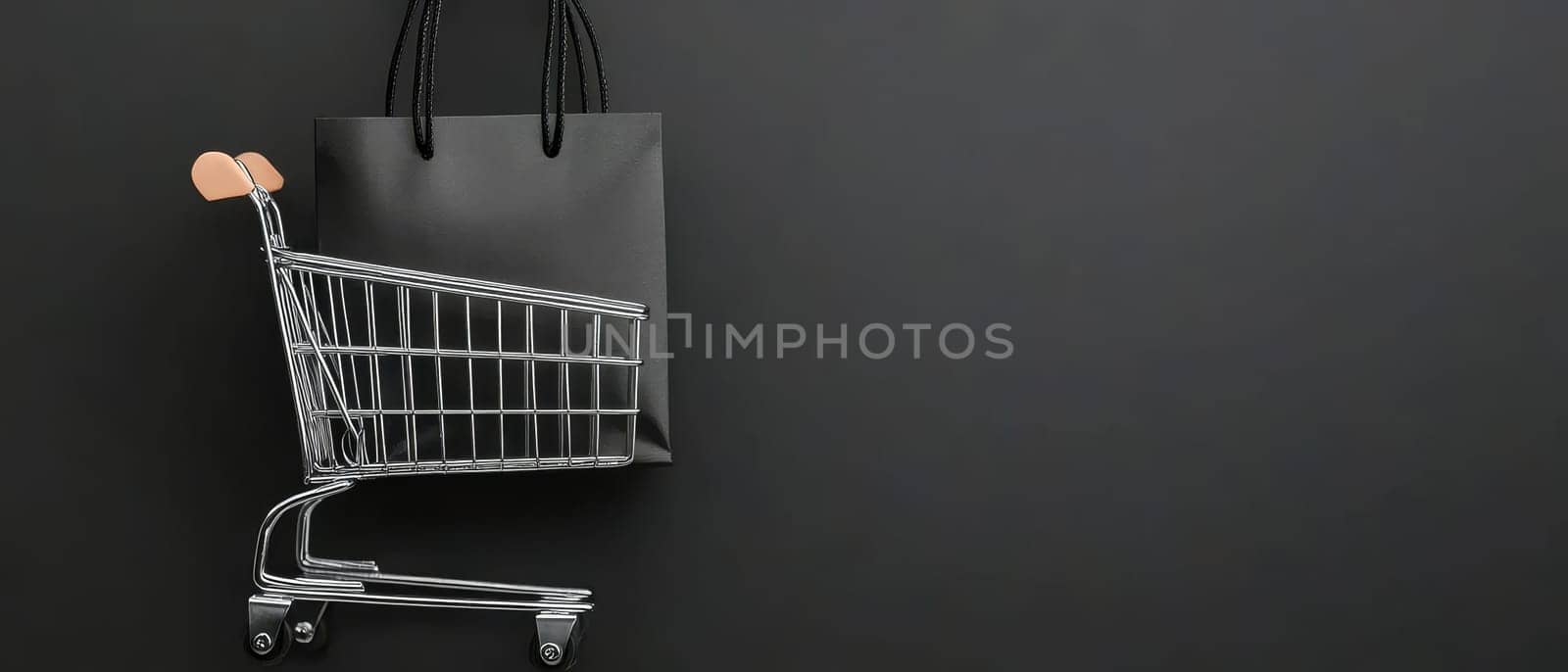 A black shopping cart with a shopping bag against a dark background, featuring copy space. Black Friday sale concept with empty place for text.