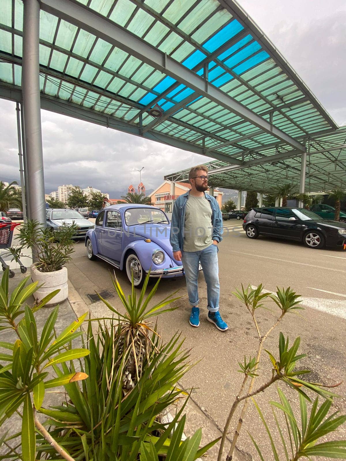 Man standing in front of vintage violet car on the street in summer. Old-fashioned nostalgia and retro style concept.