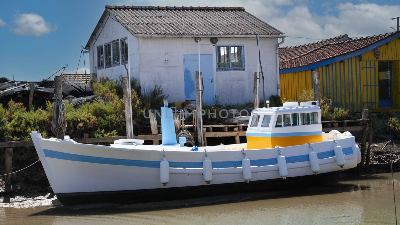 A small white boat with blue trim sits next to a house. island of Oleron, France