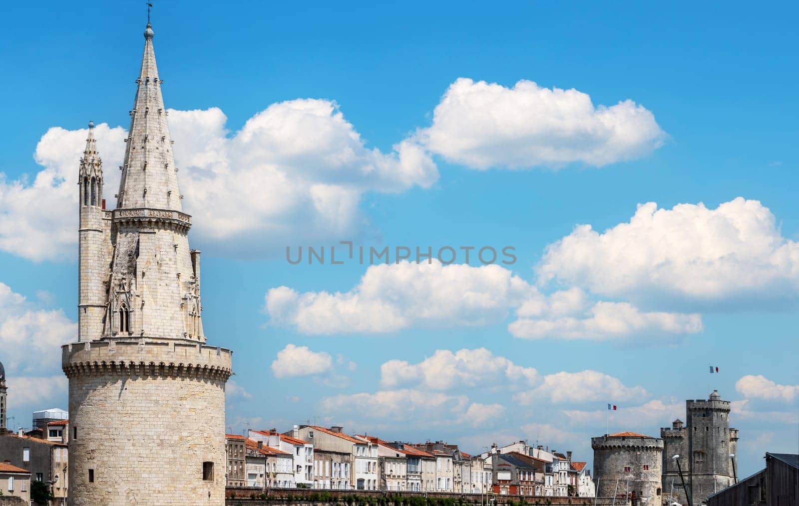 A city of La Rochelle with a tall tower and a cloudy sky. The sky is blue and the clouds are white