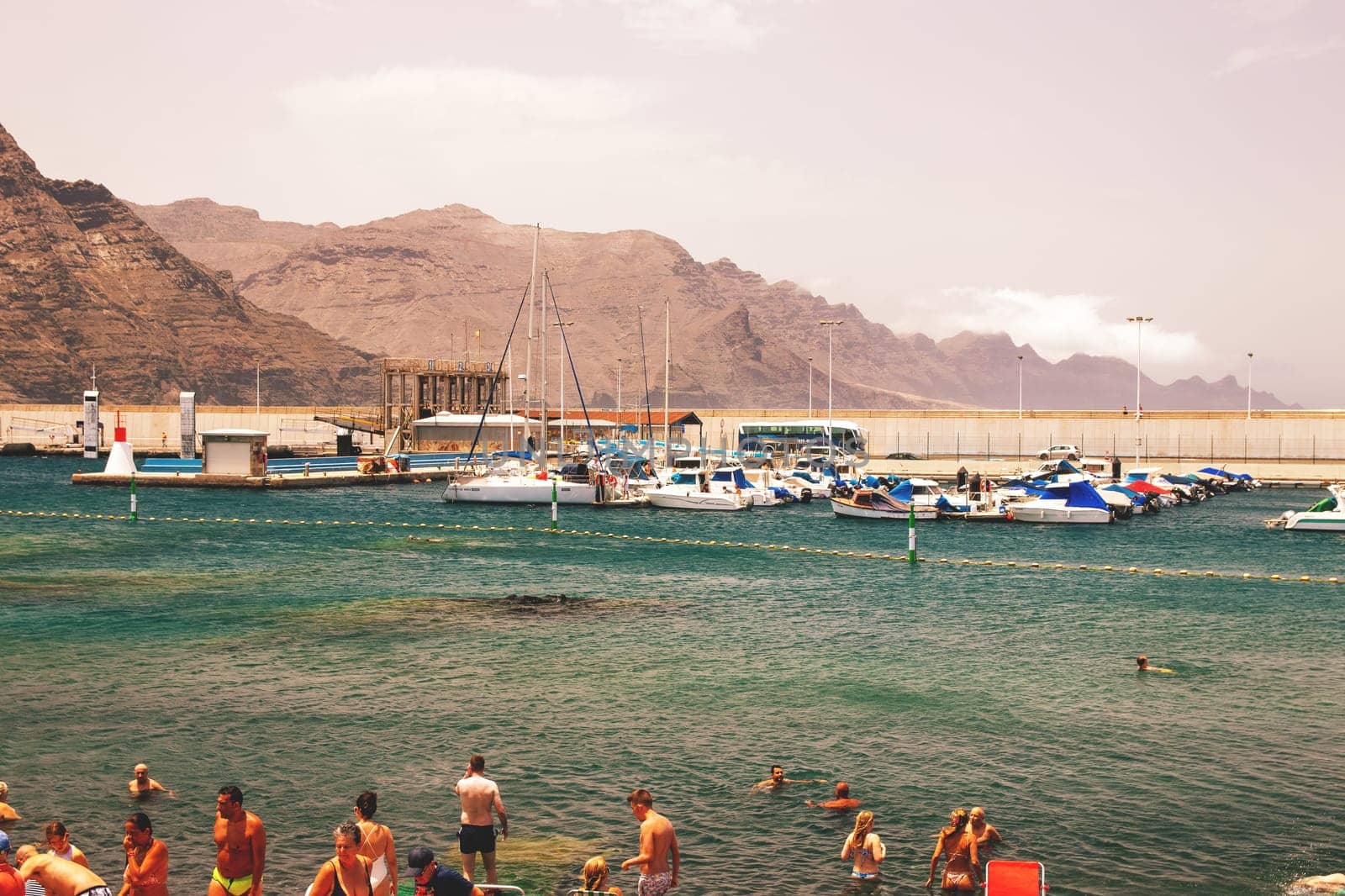 Puerto de las Nieves, Gran Canaria Island, Spain - 20 July 2024. Tourists on the stony beach Playa de las Nieves with a view of the harbour.