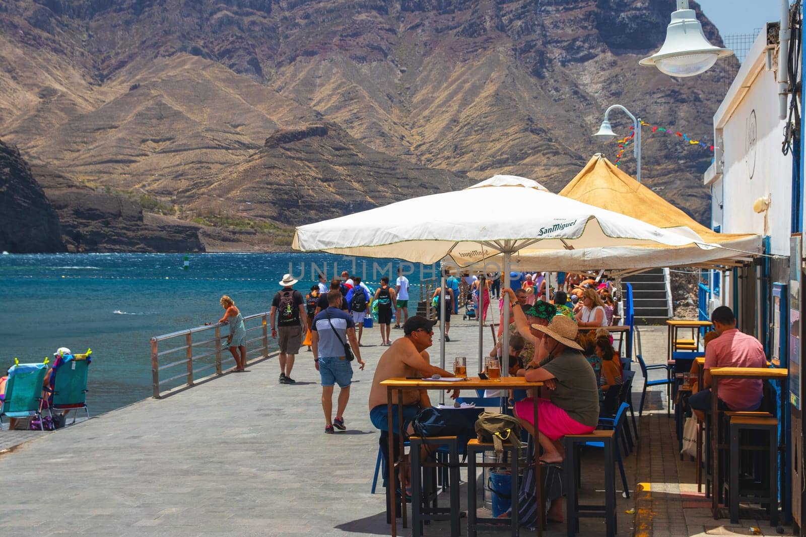 Puerto de las Nieves, island of Gran Canaria, Spain – 20 Jul 2024. Tourists and locals on the streets with typical white-blue romantic architecture port town.
