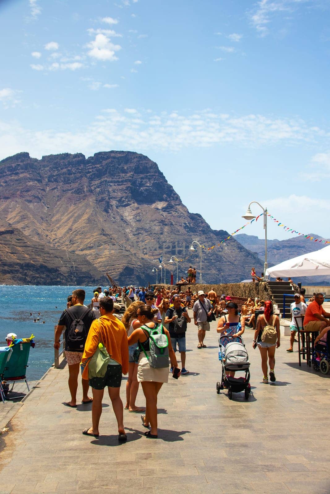 Puerto de las Nieves, island of Gran Canaria, Spain – 20 Jul 2024. Tourists and locals on the streets with typical white-blue romantic architecture port town.