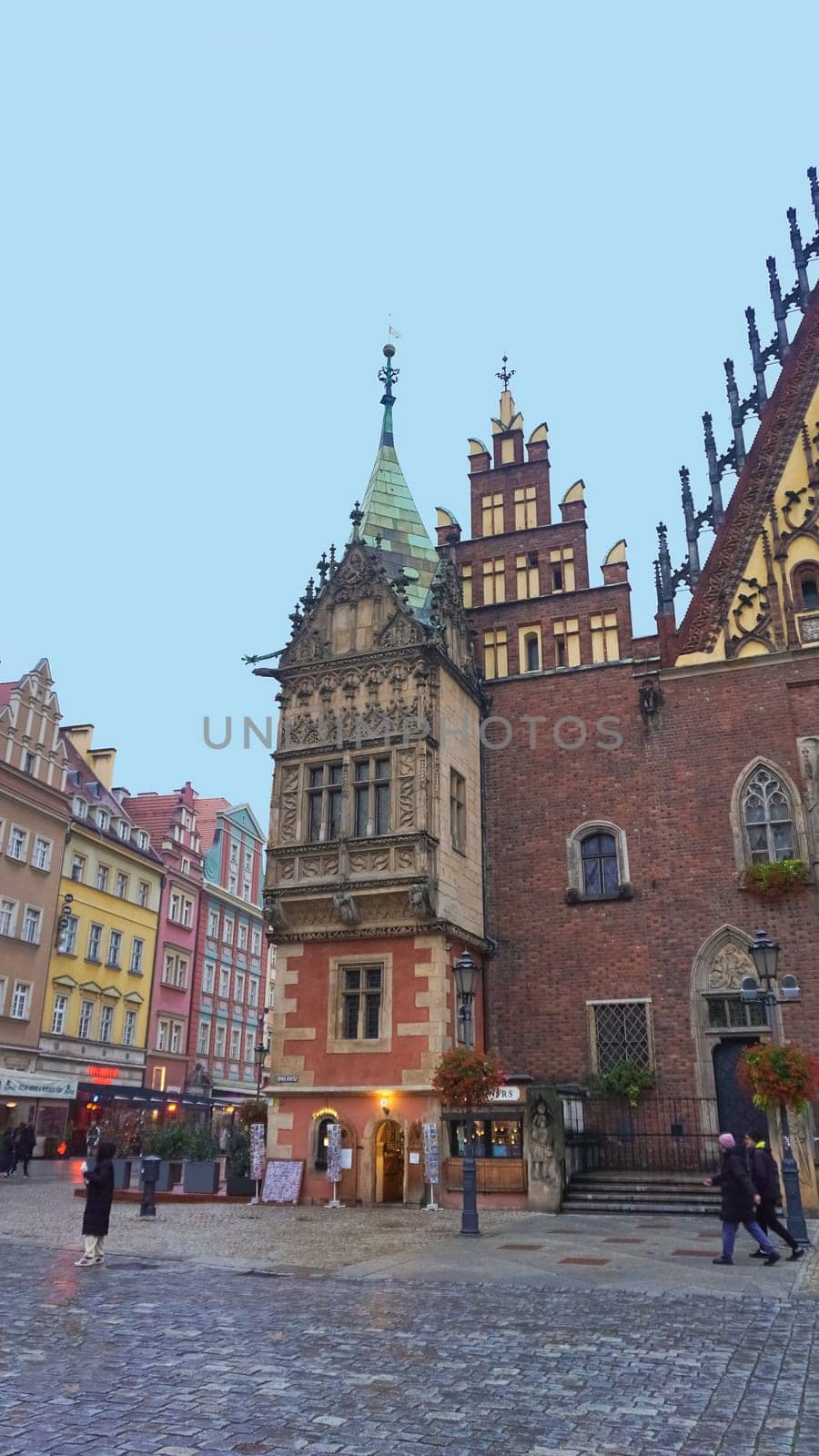 Wroclaw, Poland - April 17, 2022: The people going near old town hall building with a clock in the center of Wroclaw Square at Poland